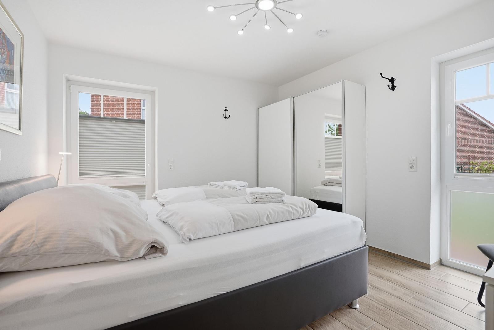 Schlafzimmer mit Bett, Spiegelschrank und Fenstern.