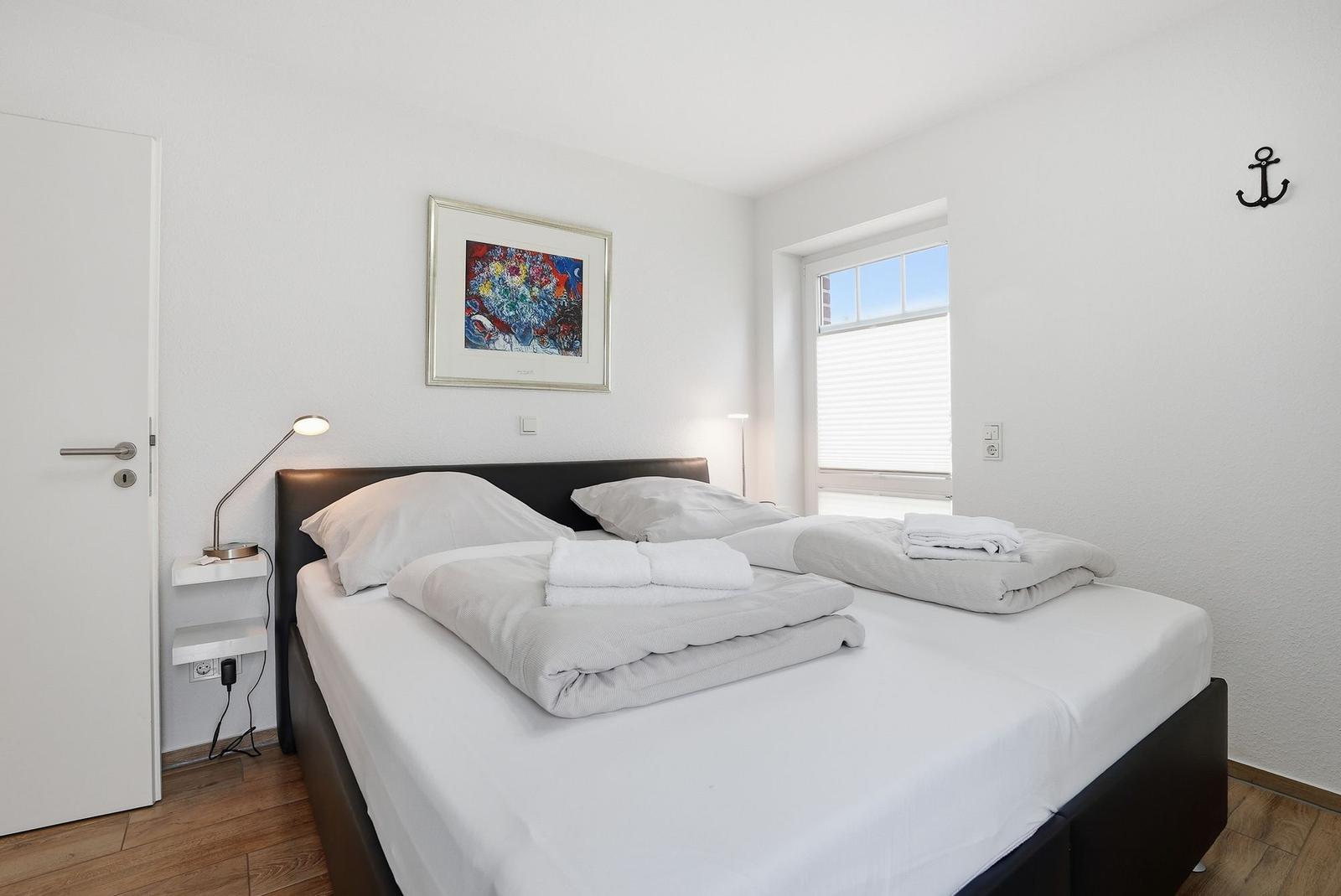 Schlafzimmer mit Bett, Fenster und Wandbild. An der Wand hängt ein Anker.