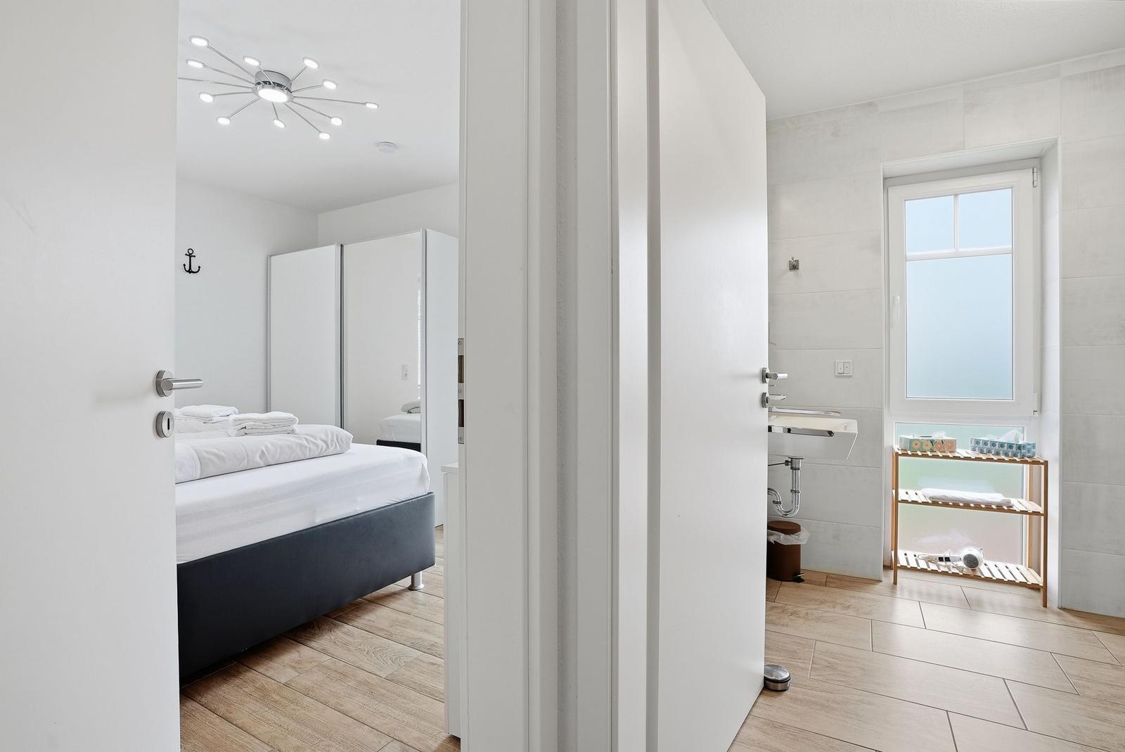 Schlafzimmer mit Bett und Kleiderschrank. Nebenraum mit Waschbecken und Fenster.