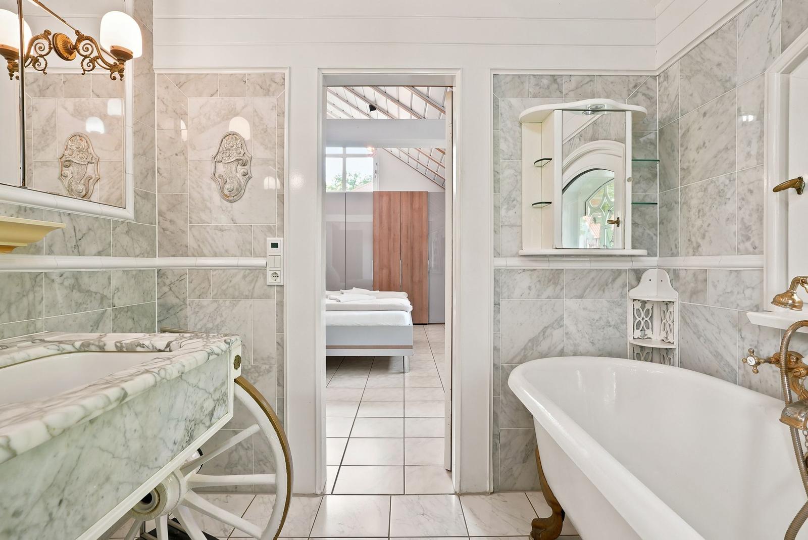 Badezimmer mit Marmorwand, Badewanne und Waschtisch mit Radgestell.