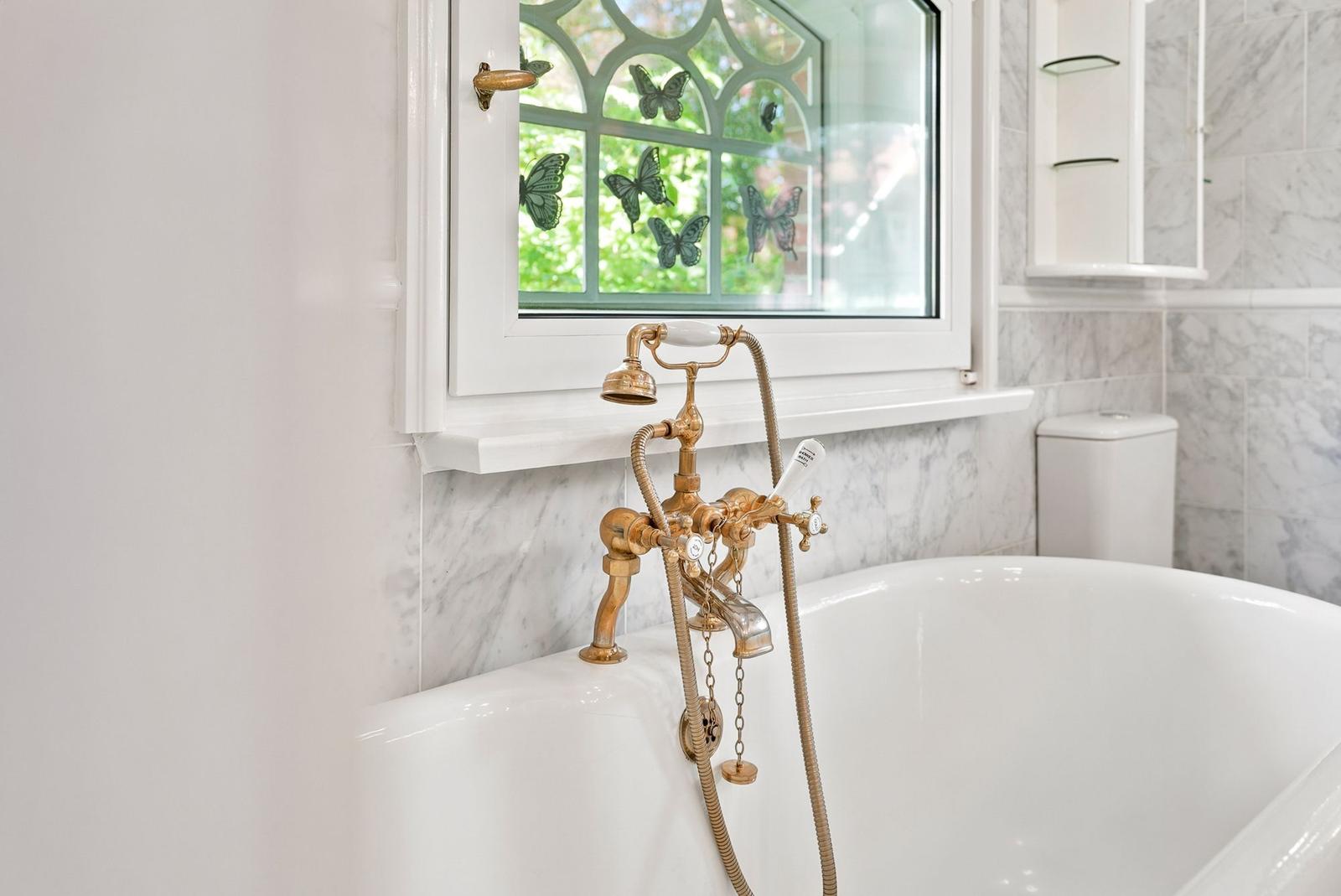 Badewanne mit goldfarbenem Wasserhahn und Fenster mit Schmetterlingsmotiven.