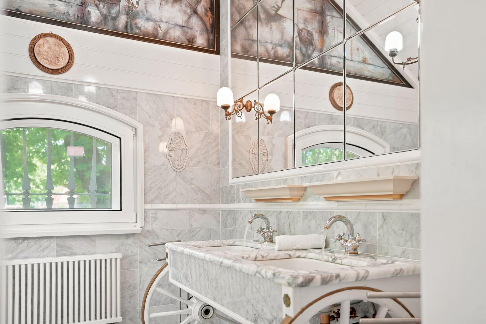 Badezimmer mit Marmor, Spiegel und Fenster. Doppelwaschbecken mit Wasserhahn.