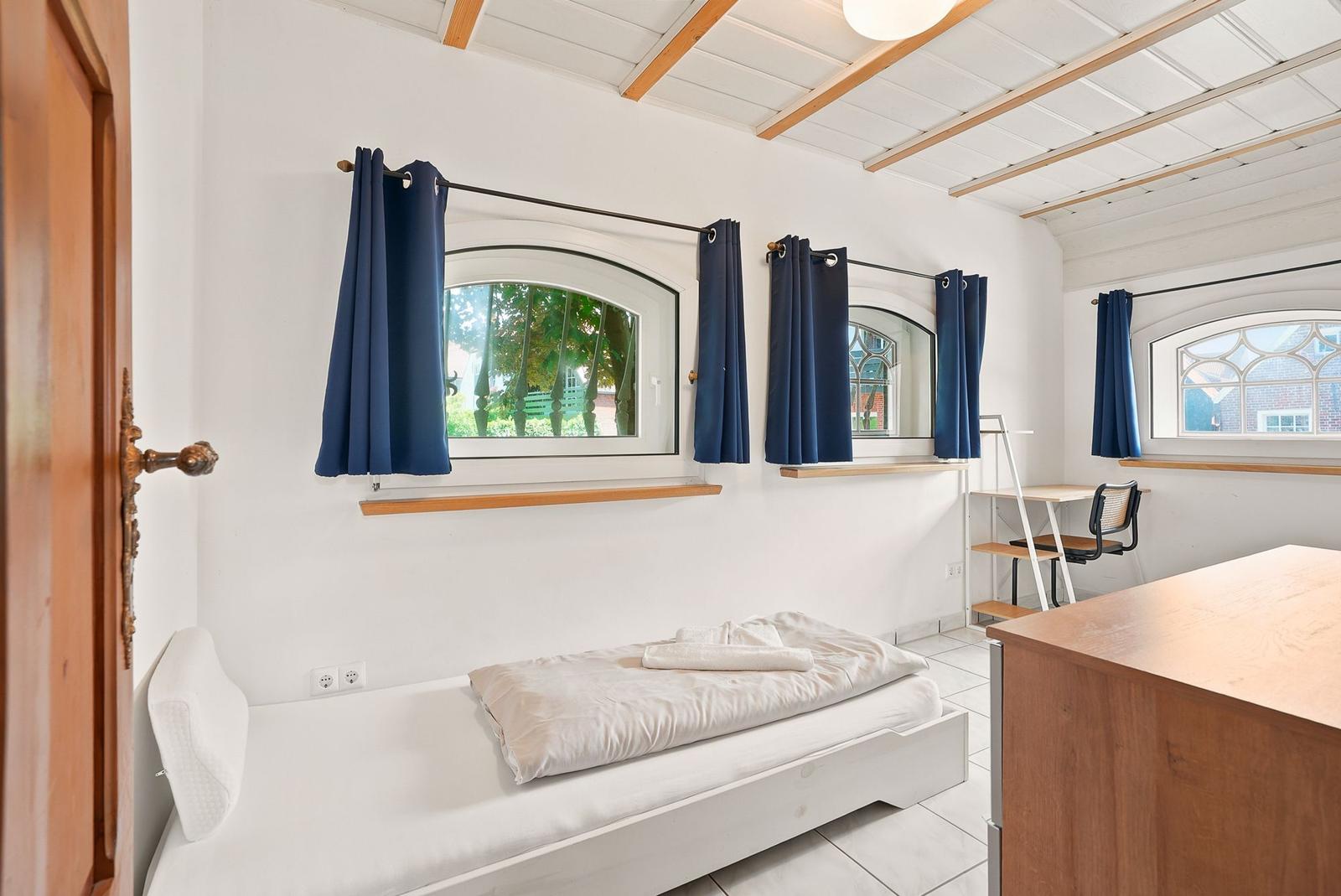 Ein Schlafzimmer mit Bett, drei Fenstern und einem Schreibtisch.