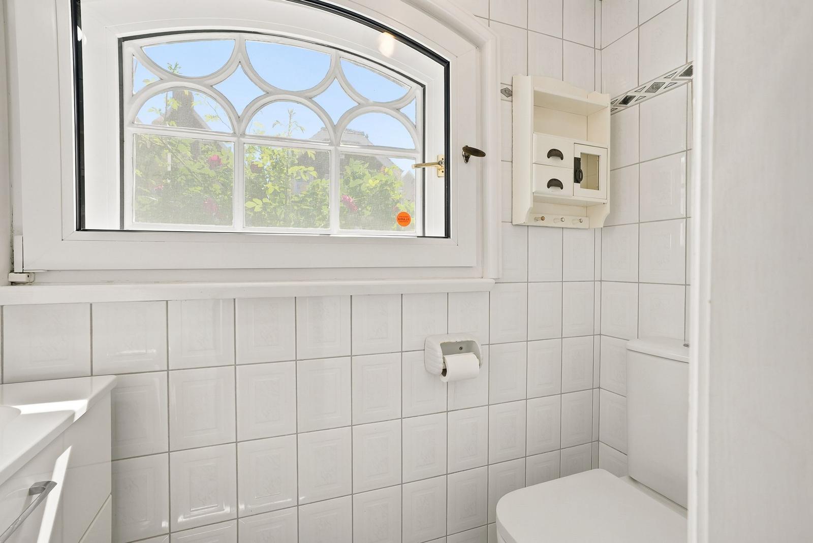 Badezimmer mit weißer Fliesenwand, Toilette und Fenster mit Bogenförmigem Glas.