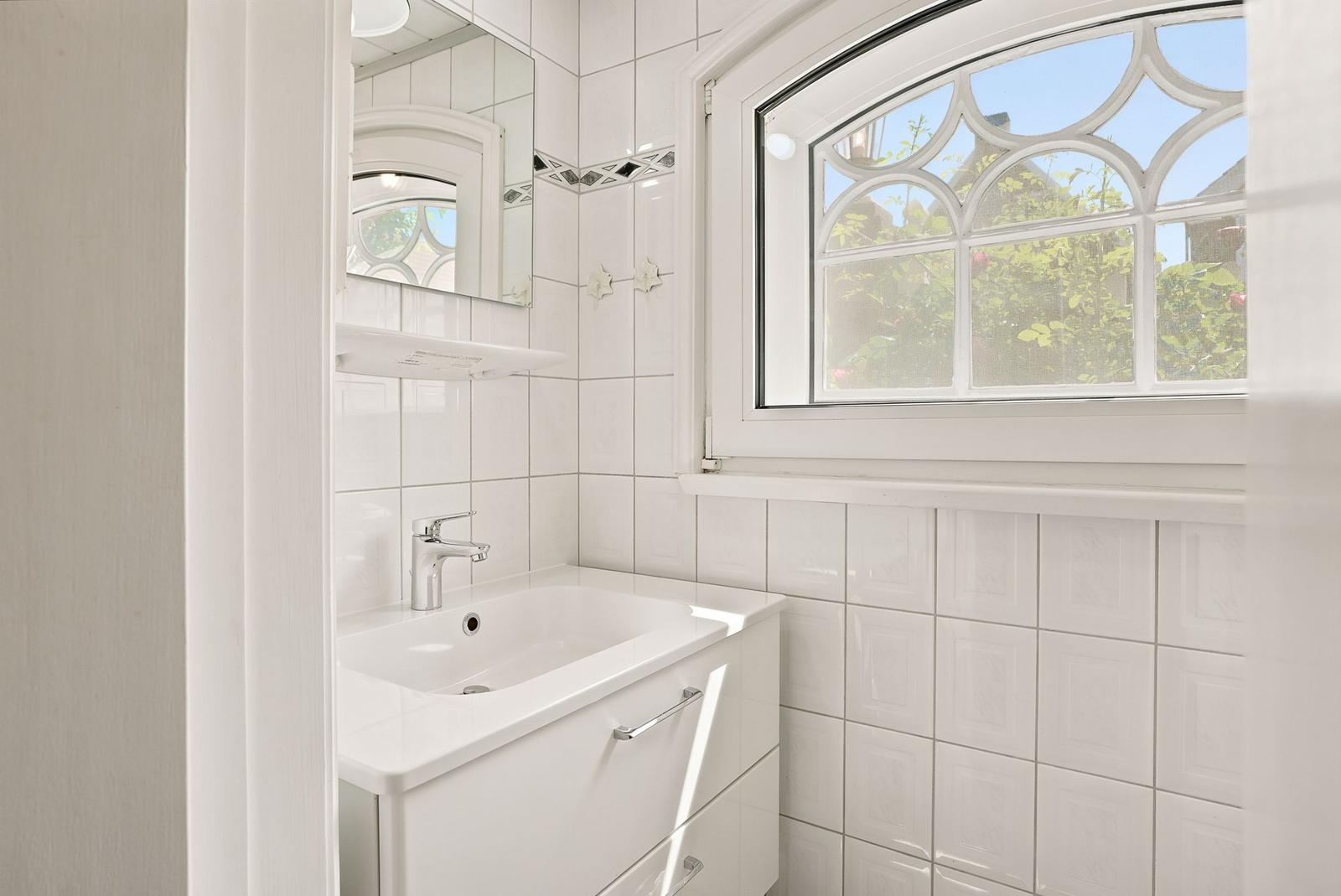 Badezimmer mit Waschbecken, Spiegel und Fenster mit gotischem Glas.