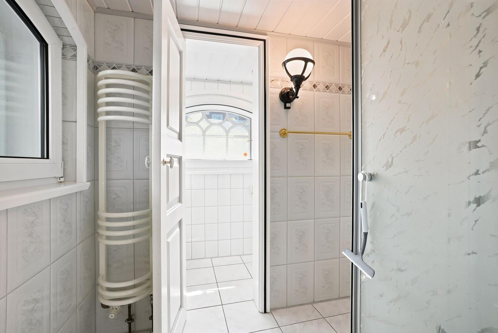 Dusche mit Glaswand, Tür zum Bad und Fenster mit Heizkörper.