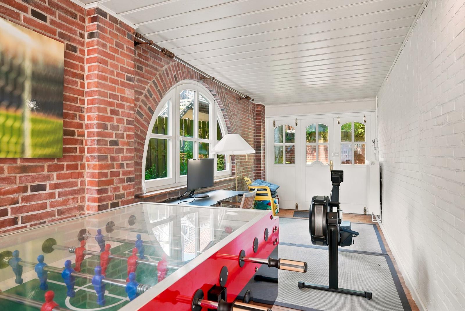 Raum mit Tischfußball, Fitnessgerät und Fenster mit Blick auf Garten.