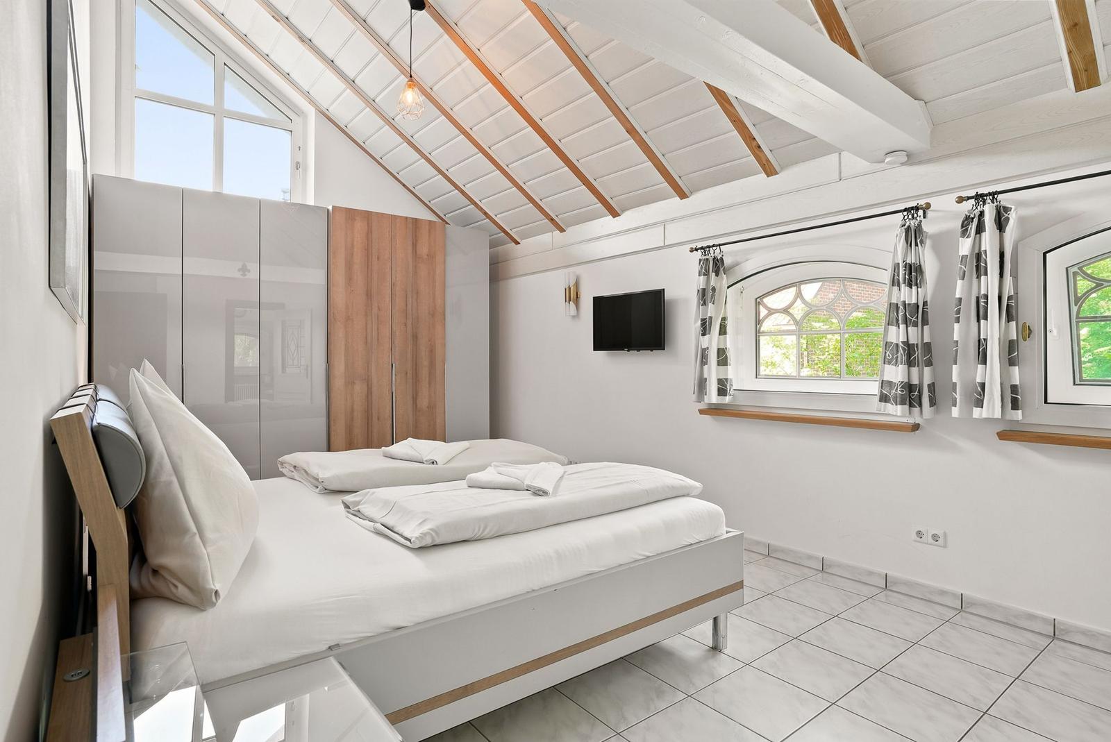 Schlafzimmer mit Doppelbett, Fenstern und TV an der Wand.