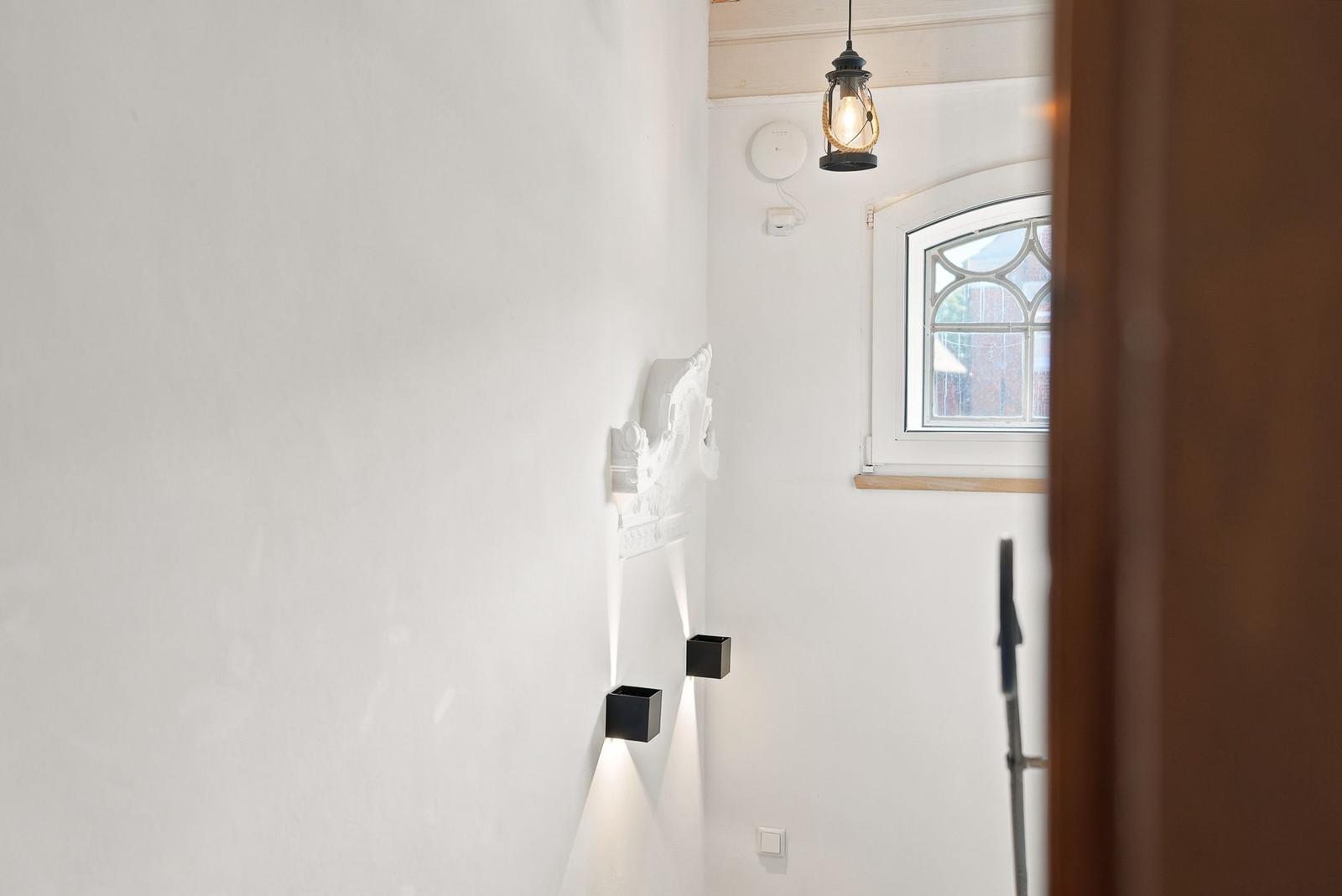 Helle Wand mit dekorativer Skulptur, schwarzen Wandlampen und Fenster mit Bogenform.