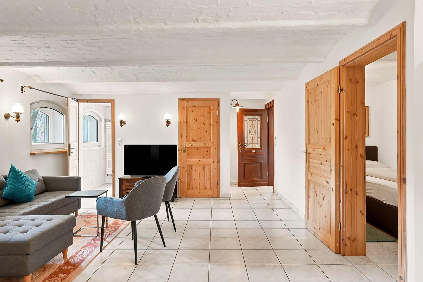 Wohnung mit Wohnzimmer, Fernseher und Schlafzimmer. Holztüren und weißer Kalkputzdecke.