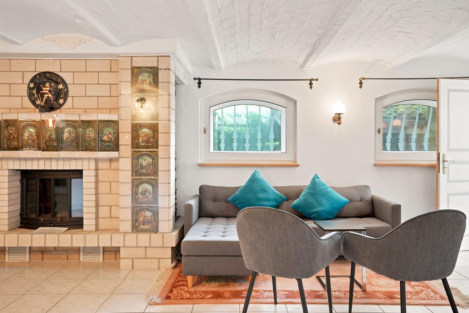 Wohnzimmer mit Sofa, zwei Stühlen, Kamin und zwei Fenstern.