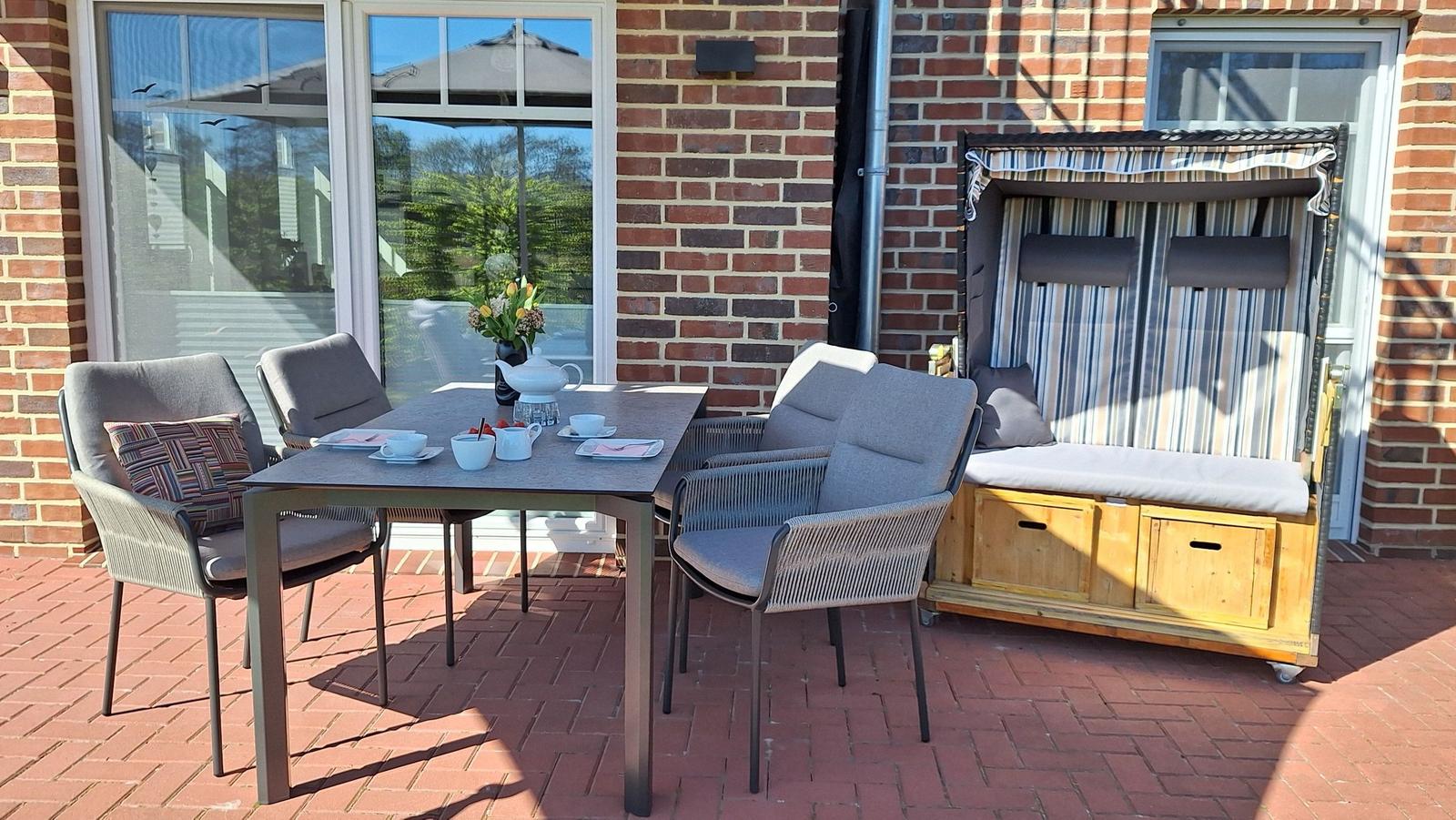 Terrasse mit Tisch, Stühlen und Strandkorb. Roter Steinboden und Backsteinmauer.