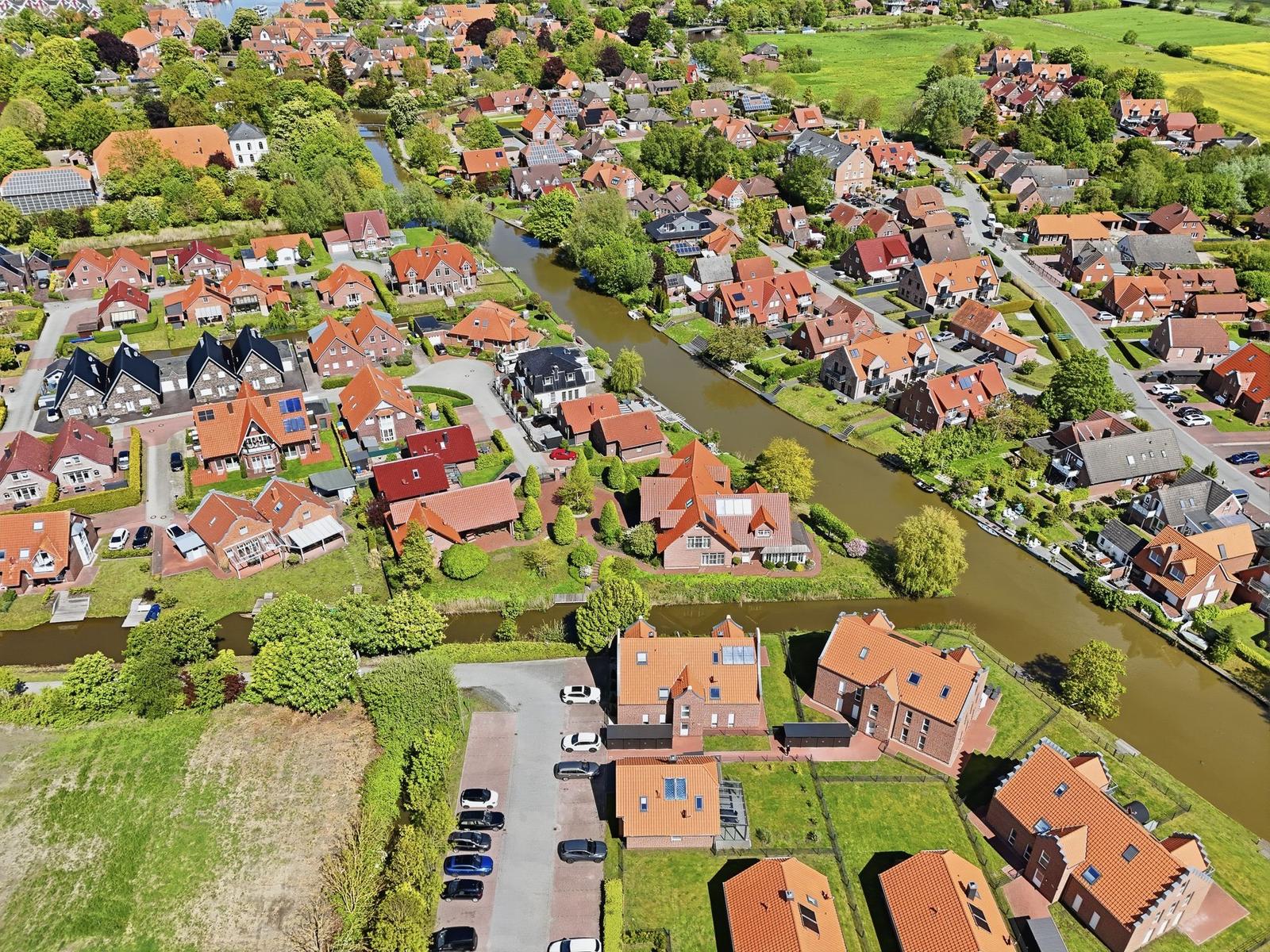 Aerial view of a village with red-tiled roofs, green lawns, and a winding canal.