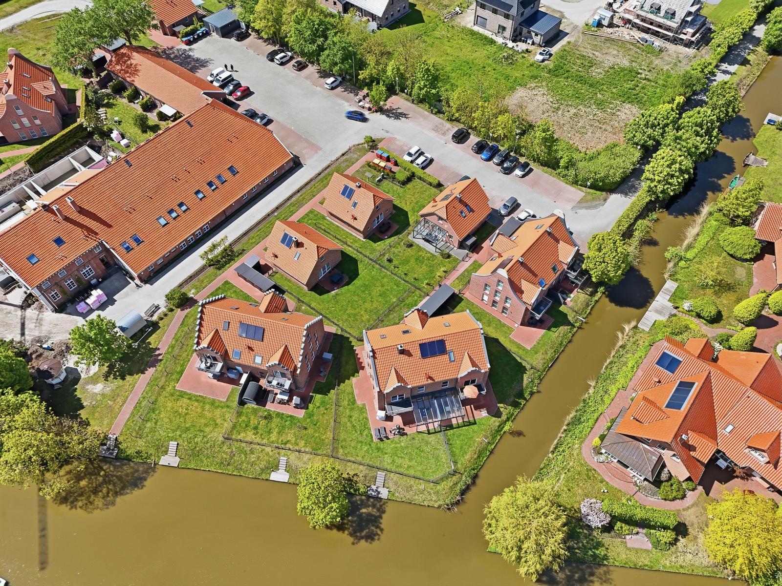 Luftbild von Häusern mit roten Dächern und grünen Gärten am Kanal.