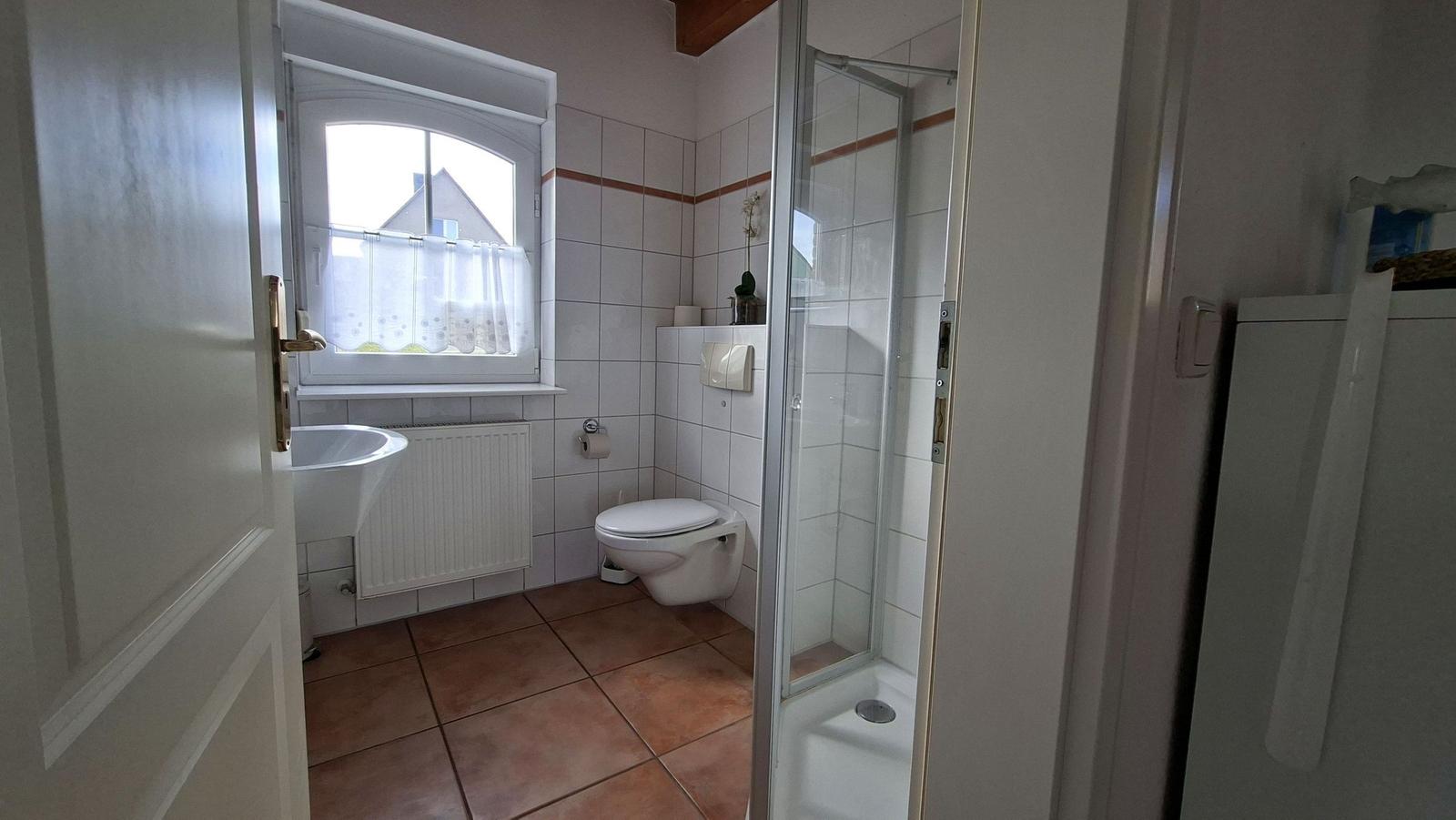 Bathroom with shower, toilet, and sink. Window with curtain.