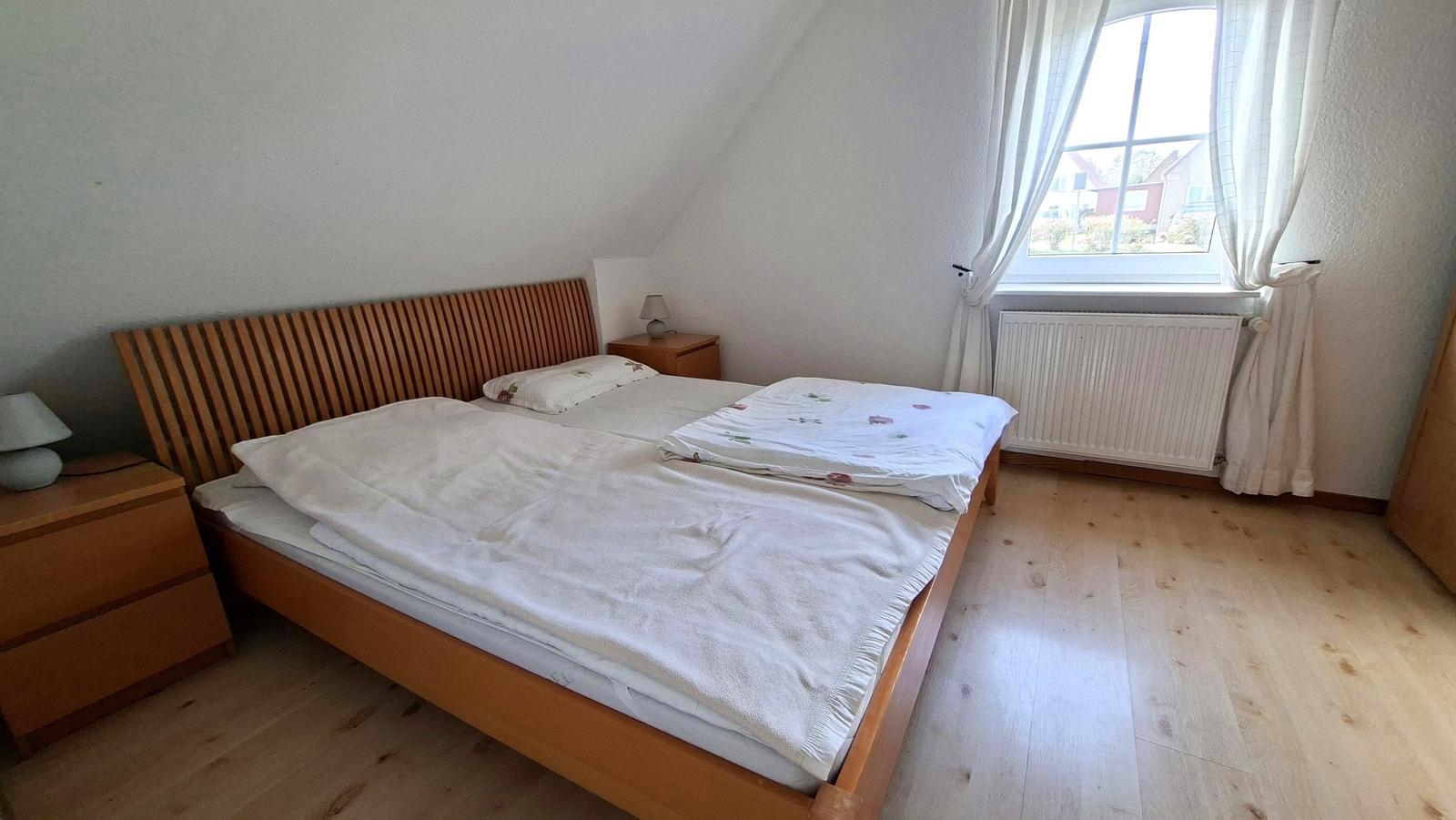 Bedroom with double bed, wooden floor, and window with view outside.