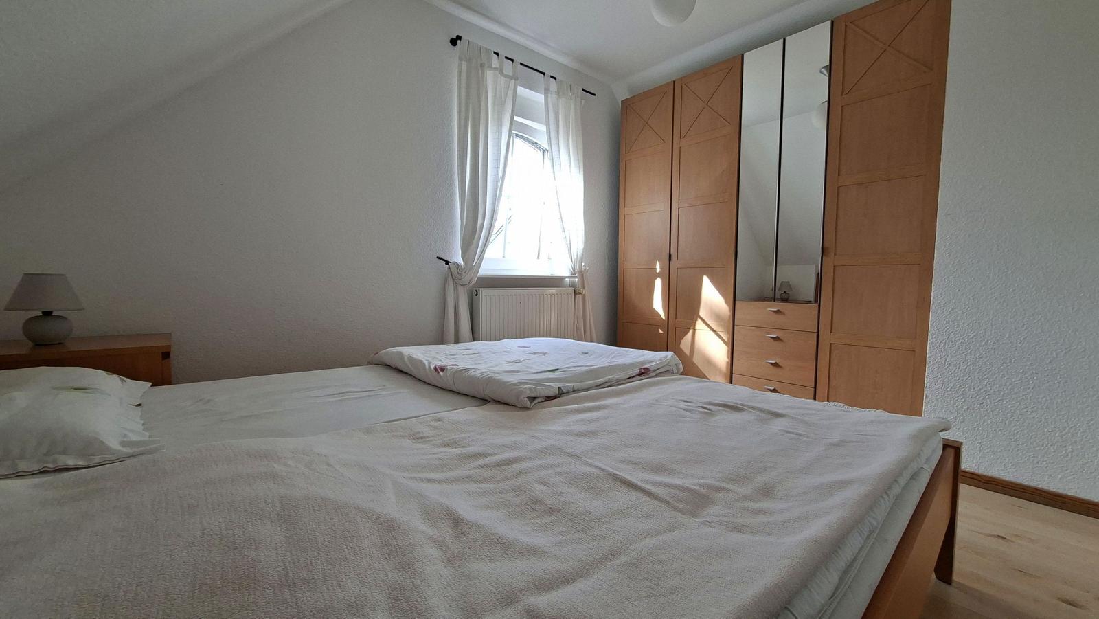 Bedroom with double bed, wardrobe, and window with white curtains.