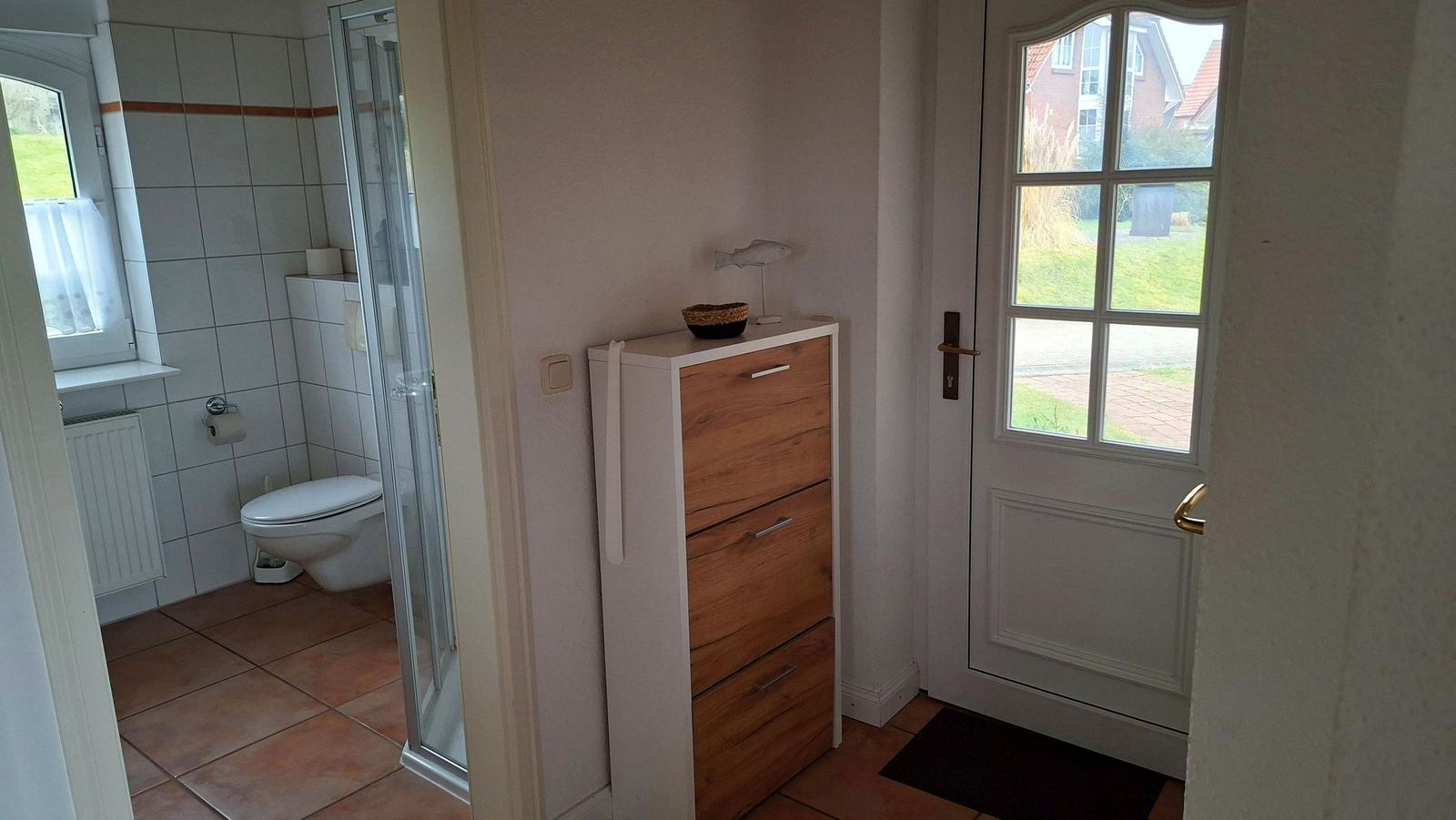 Hallway with cabinet, door, and view into toilet with shower.