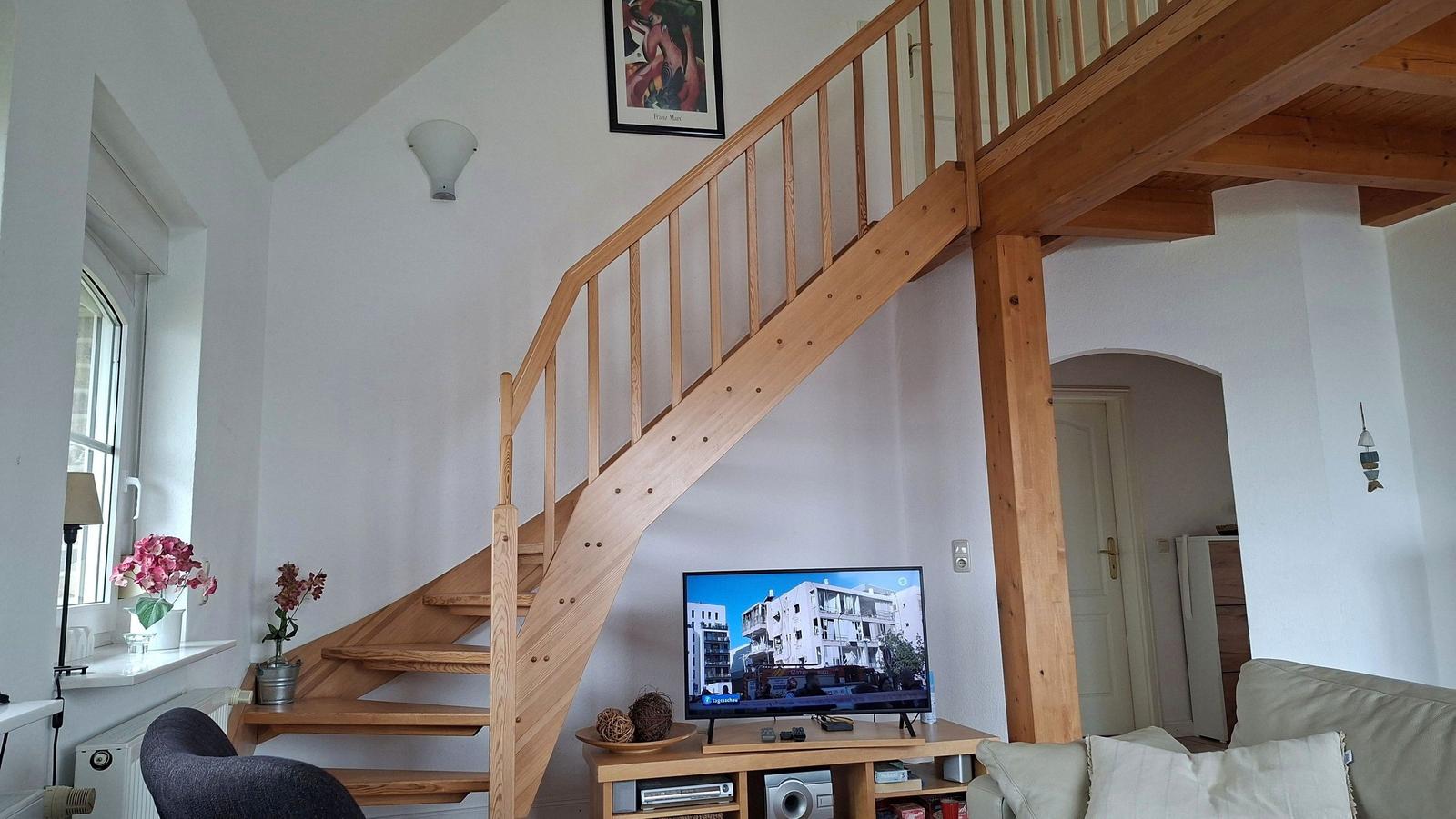 Wooden staircase leads to upper level. Living room with TV and sofa.