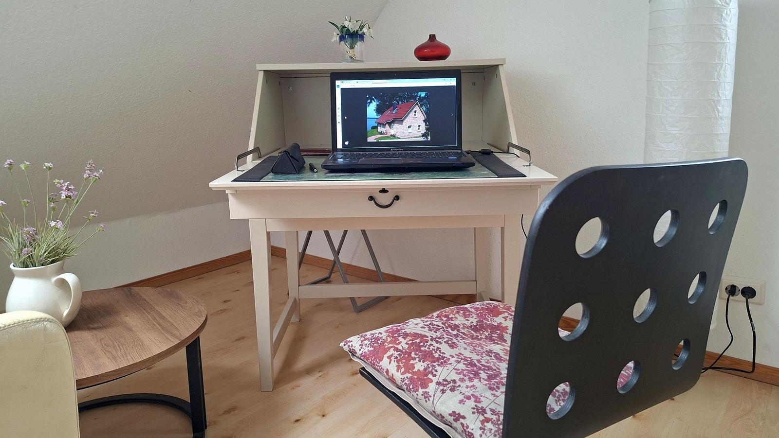 Desk with laptop and chair in a room with wooden floor and wall covering.