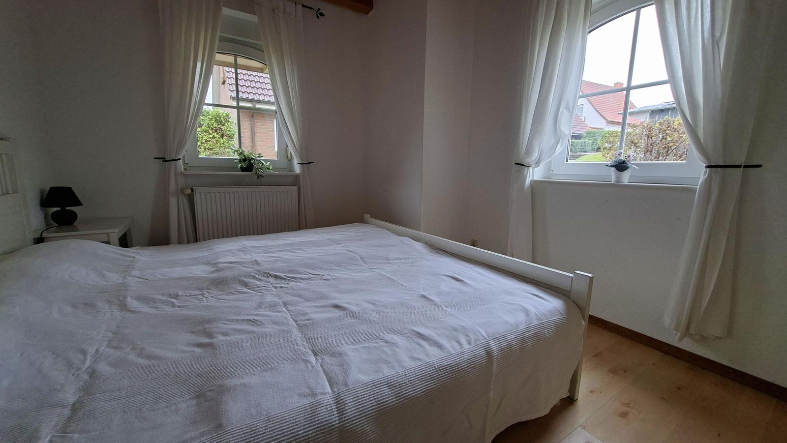 Bedroom with double bed, two windows, and wooden floor.