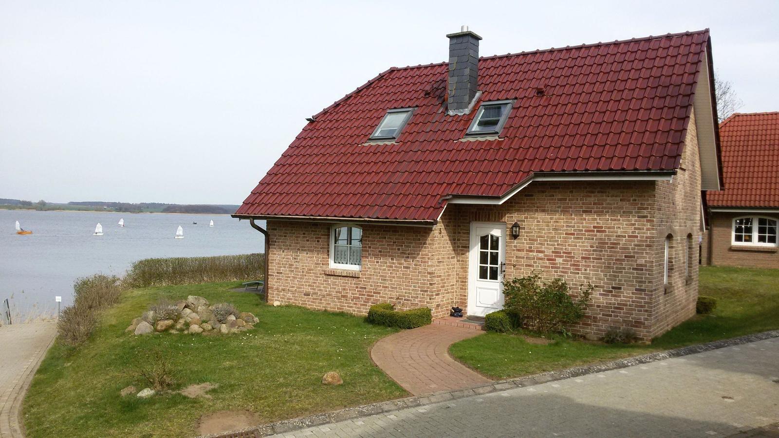 A house with a red roof and brick facade by the water with sailboats.