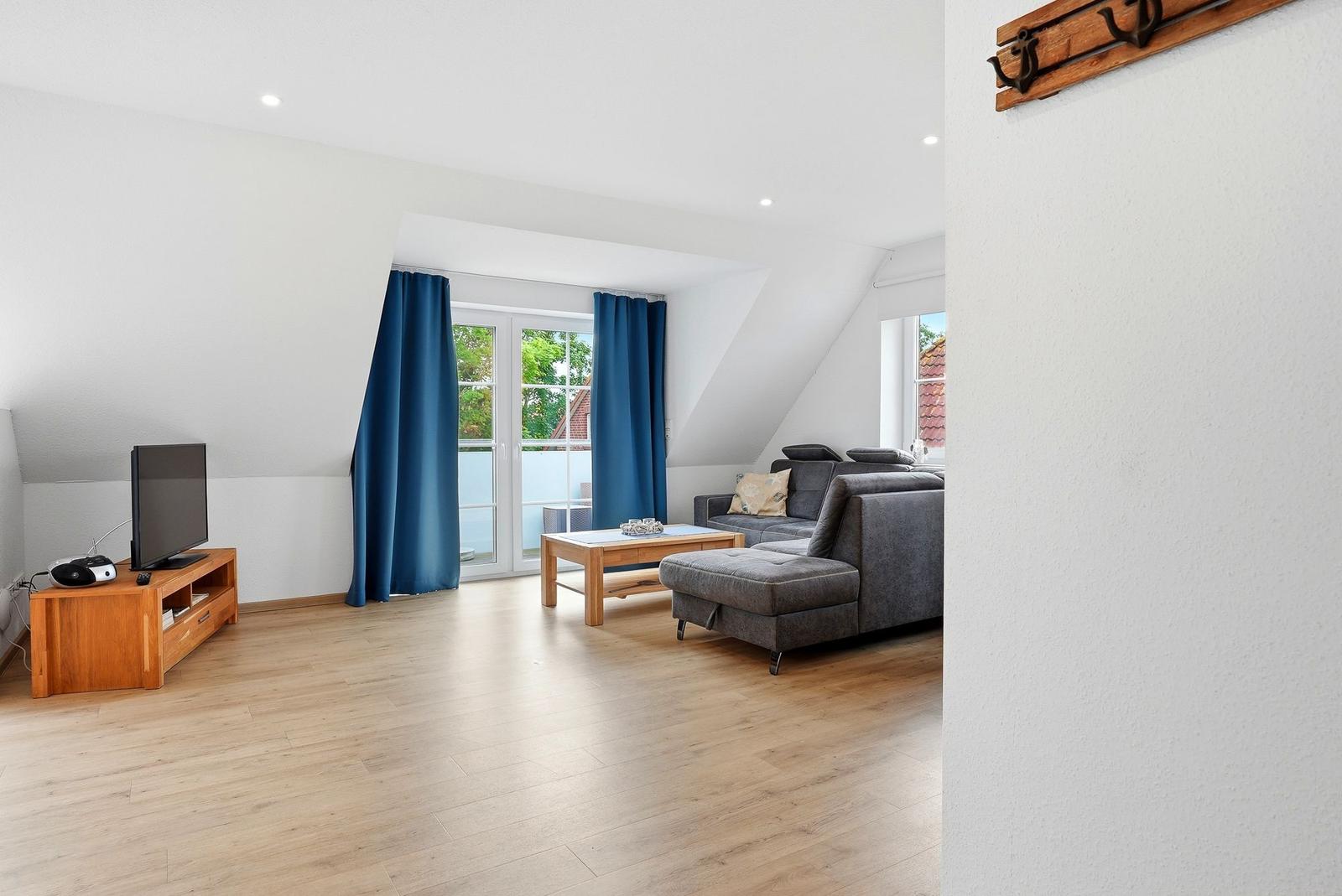 Wohnzimmer mit Sofa, Couchtisch und TV. Blaue Vorhänge vor Fenster.