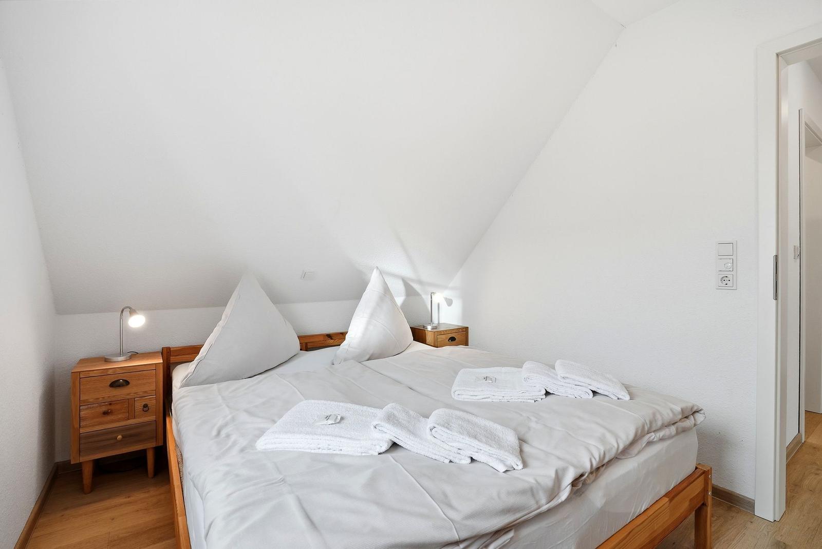 Schlafzimmer mit Doppelbett, zwei Nachttischen und gefalteten Handtüchern.