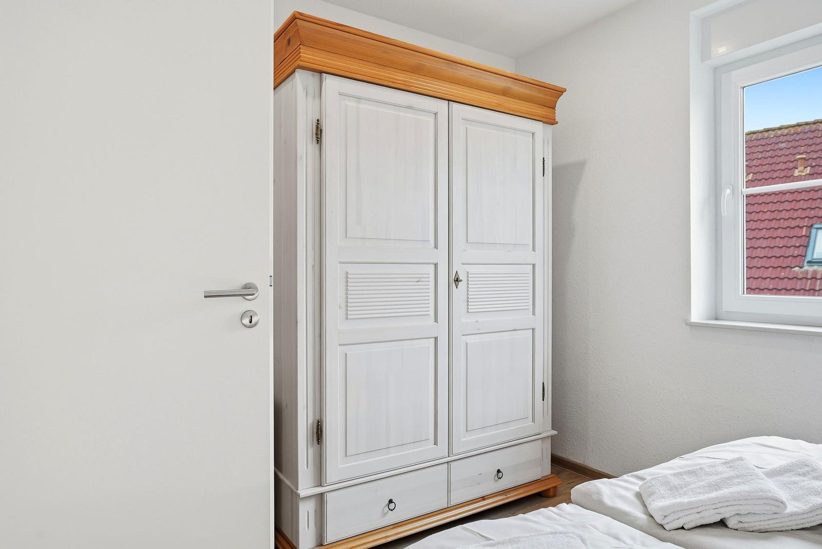 Schlafzimmer mit weißem Schrank, Bett und Fenster mit Blick auf Dach