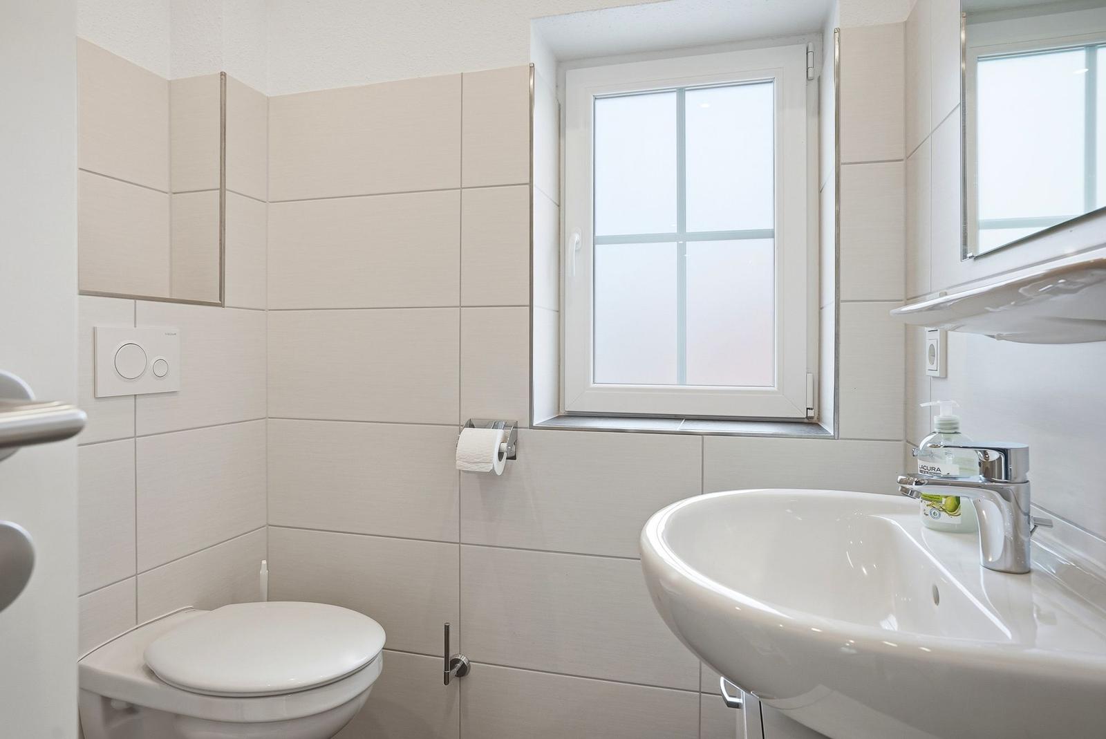 Badezimmer mit Toilette, Waschbecken und Fenster.