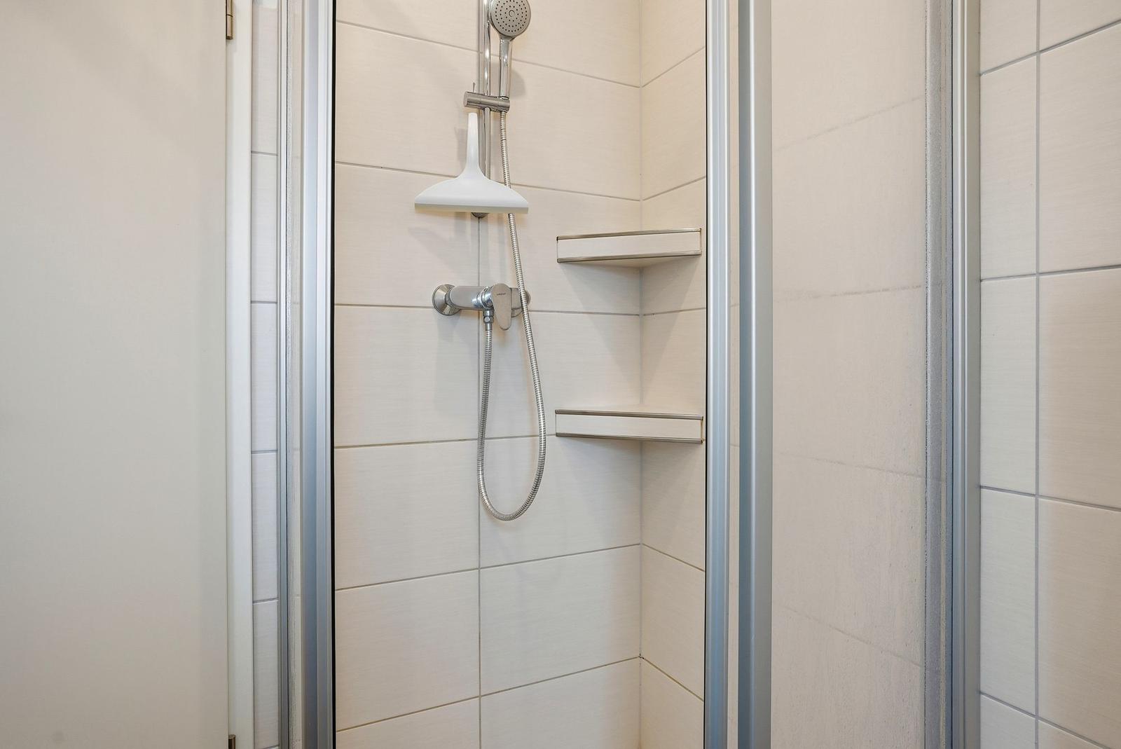 Duschkabine mit Duschbrause, Handbrause und zwei Regalen an der Wand.