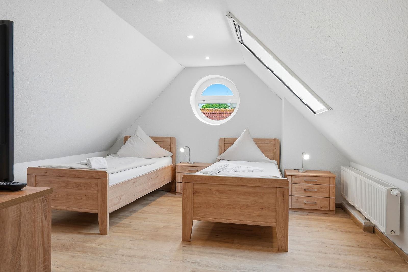 Zwei Betten mit Nachttischen unter einem Dachfenster und runden Fenster.