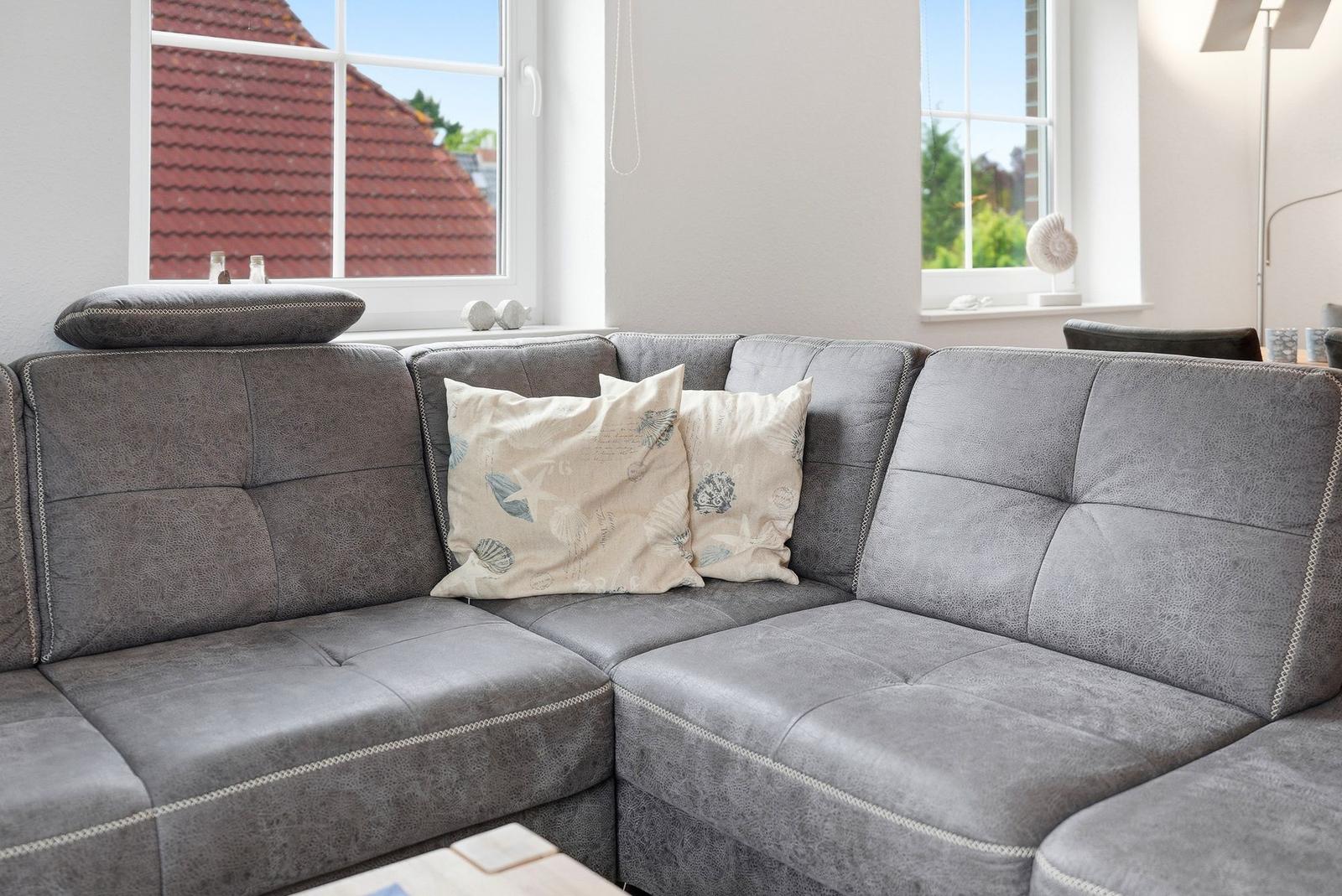 Ein grauer Ecksofa mit Kissen und Fenstern im Hintergrund.
