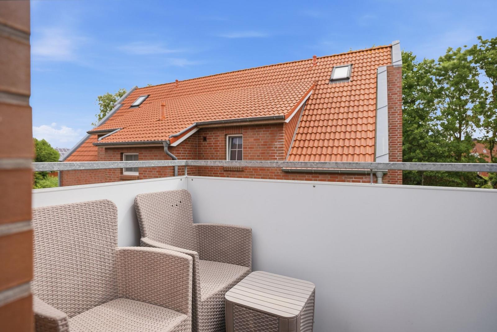Terrasse mit zwei Sitzgelegenheiten und Blick auf ein Haus mit rotem Dach.