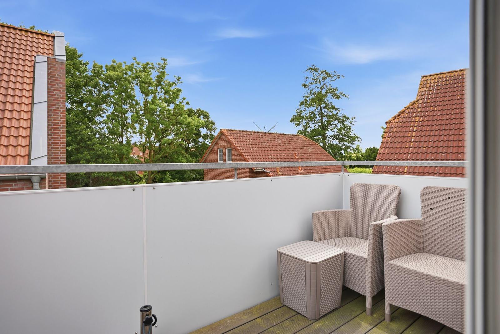 Terrasse mit zwei Stühlen und Tisch, Blick auf Dächer und Bäume.