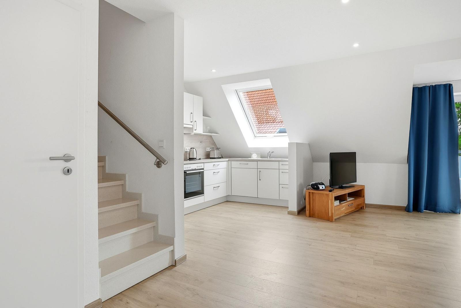 Wohnküche mit Dachschrägen, TV, Fenster und Treppe zur oberen Etage.