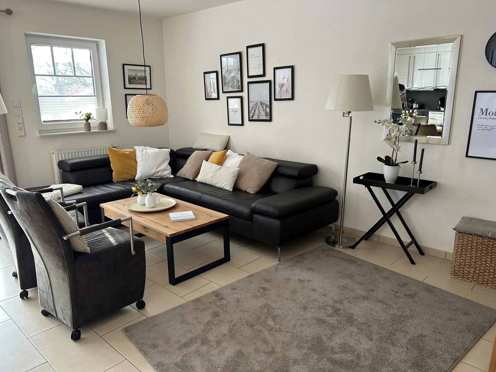 Wohnzimmer mit schwarzer Couch, Holztisch und Wanddekoration.