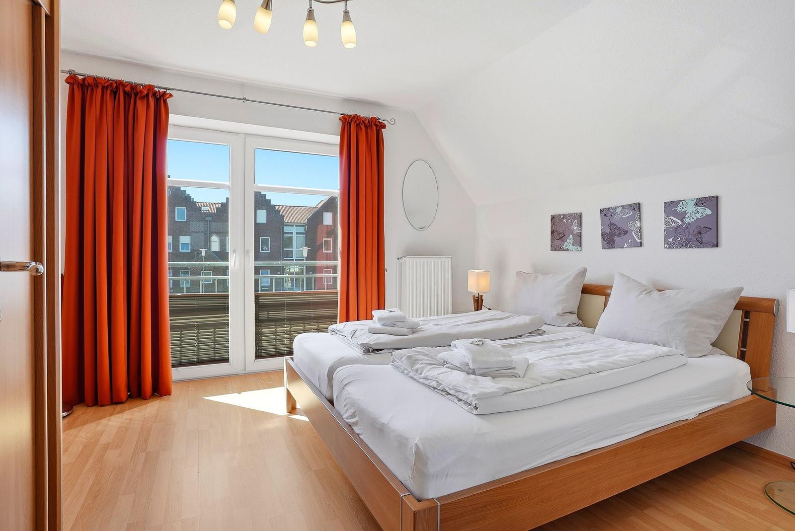 Schlafzimmer mit Doppelbett, roten Vorhängen und Balkonansicht.