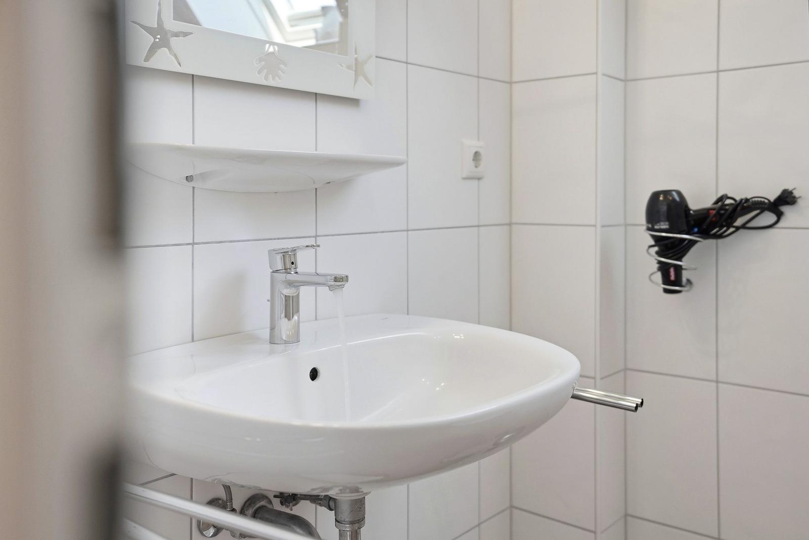 Badezimmer mit Waschbecken, Spiegel und Handtuchhalter. Duschbereich ist nicht sichtbar.