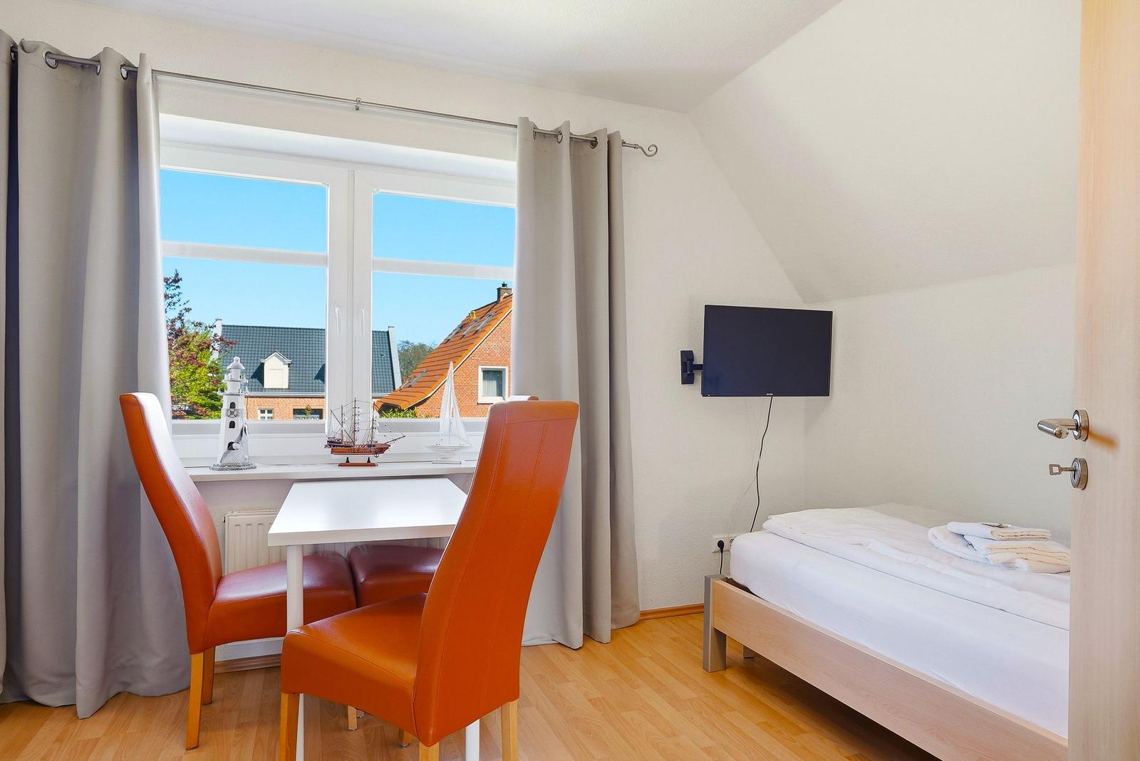 Zimmer mit Bett, Tisch, zwei Stühlen und Fenster mit Blick auf Dächer.