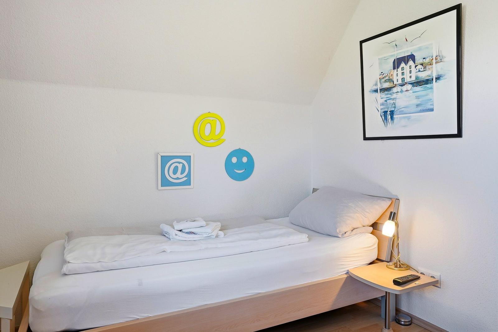 Ein Bett mit weißer Bettwäsche, Wanddekoration und Nachttisch mit Lampe.