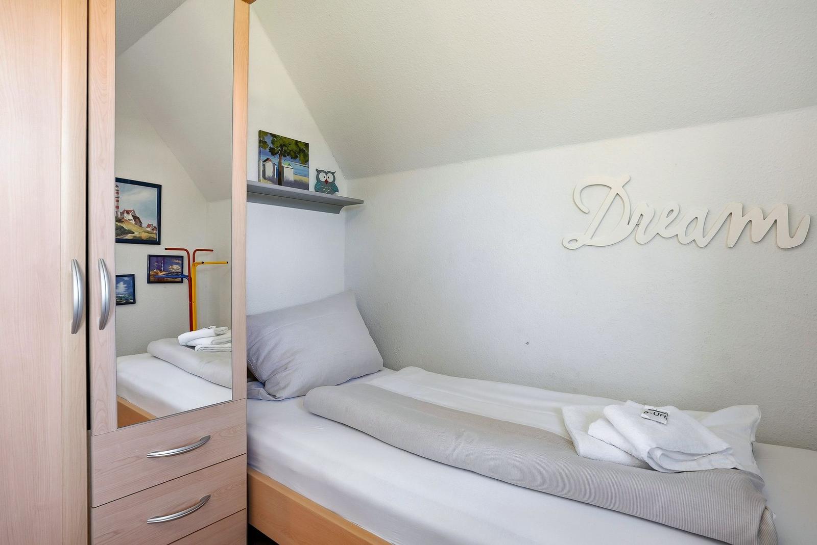 Ein Schlafzimmer mit Einzelbett, Spiegelschrank und Wanddekoration.