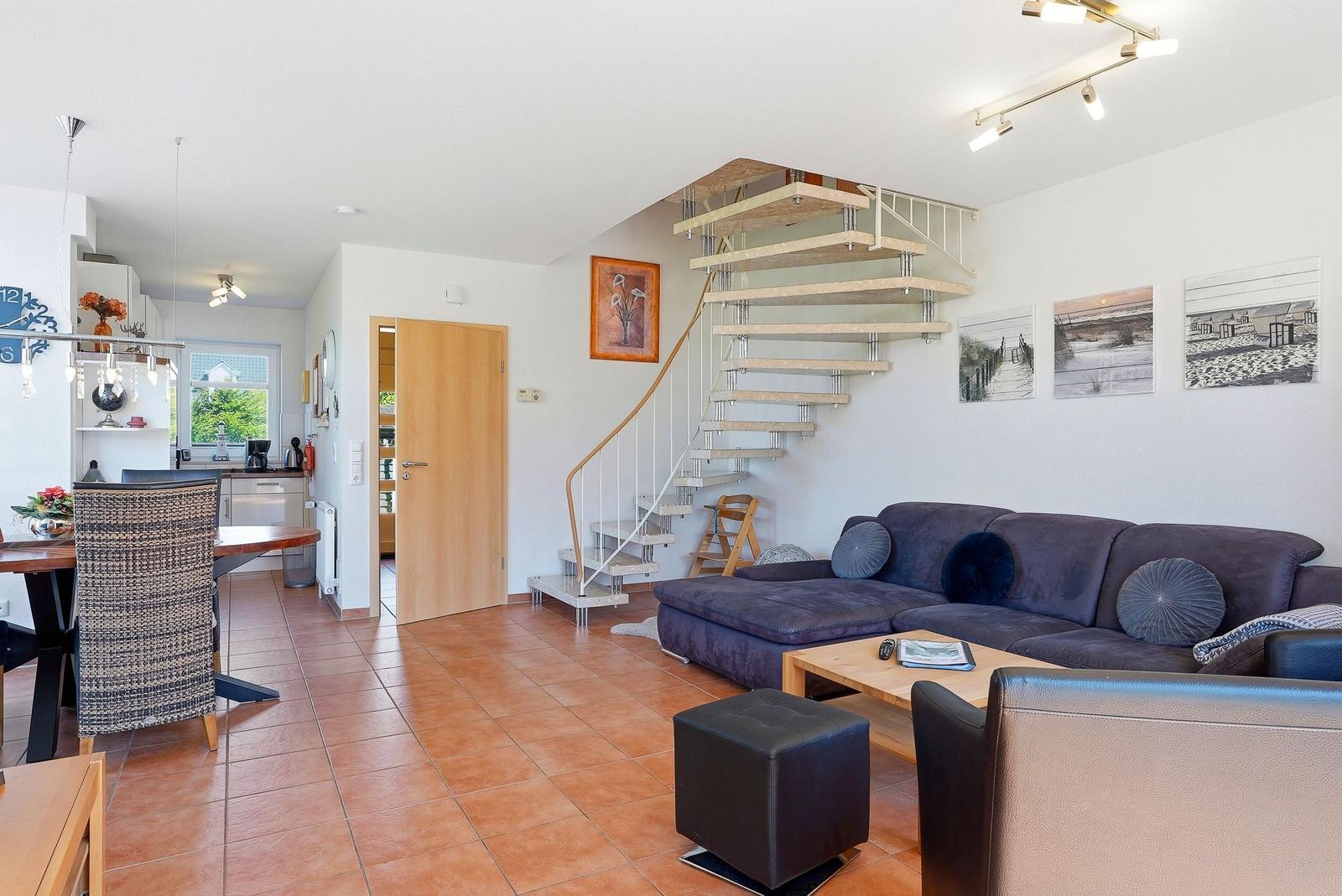 Wohnbereich mit Sofa, Treppe und Essbereich. Terrakottafußboden und weiße Wände.