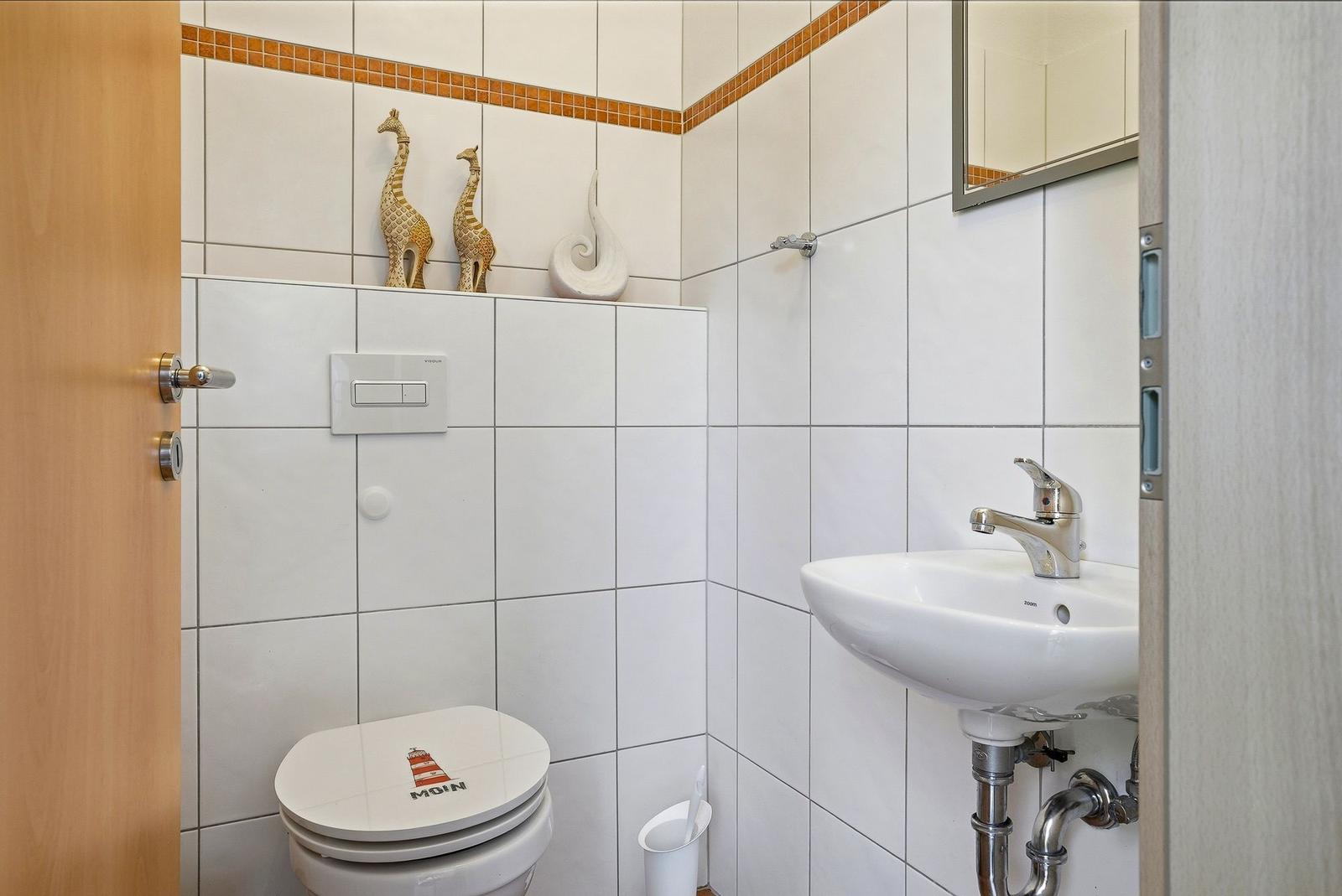 Badezimmer mit Toilette, Waschbecken und Dusche. Wandfliesen und dekorative Giraffenfiguren.