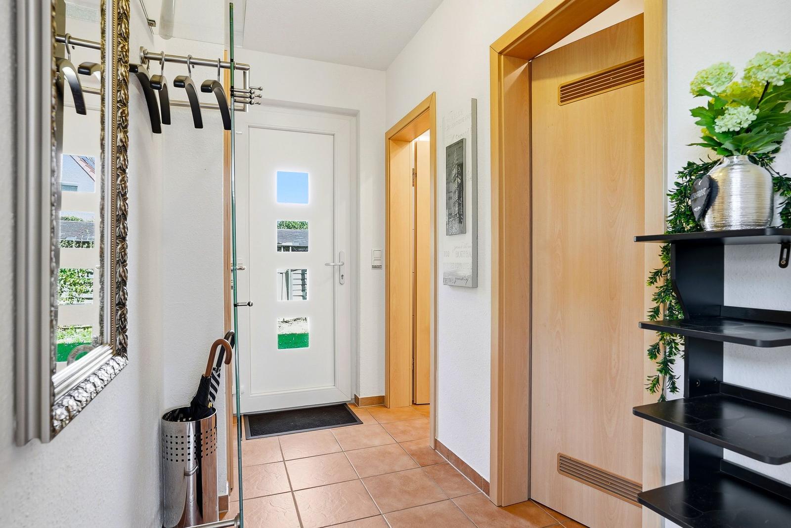 Eingangsbereich mit Garderobe, Spiegel und Tür. Holztüren und Fliesenboden.