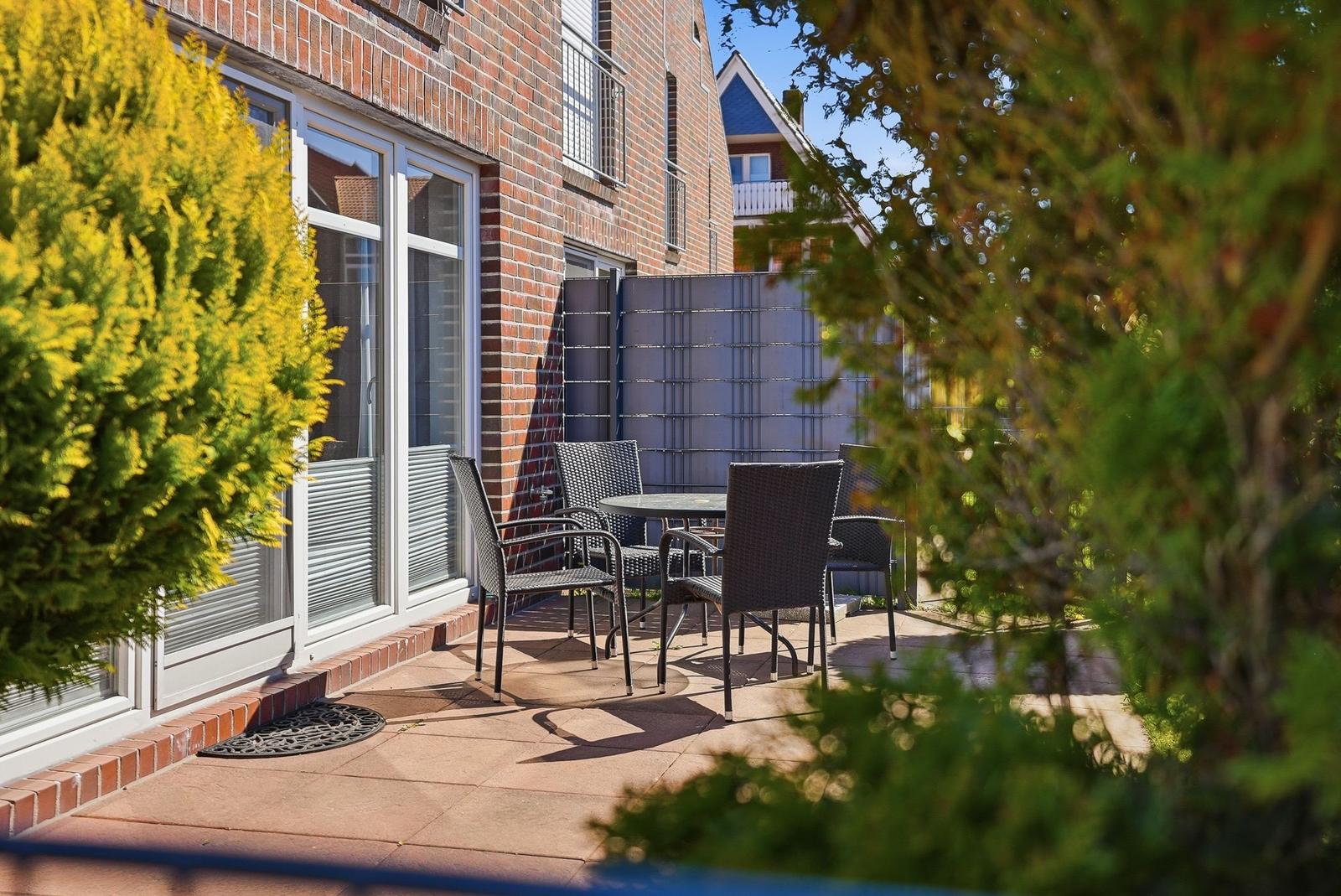 Terrasse mit Tisch und Stühlen vor einem Haus mit Fenster und Zaun.