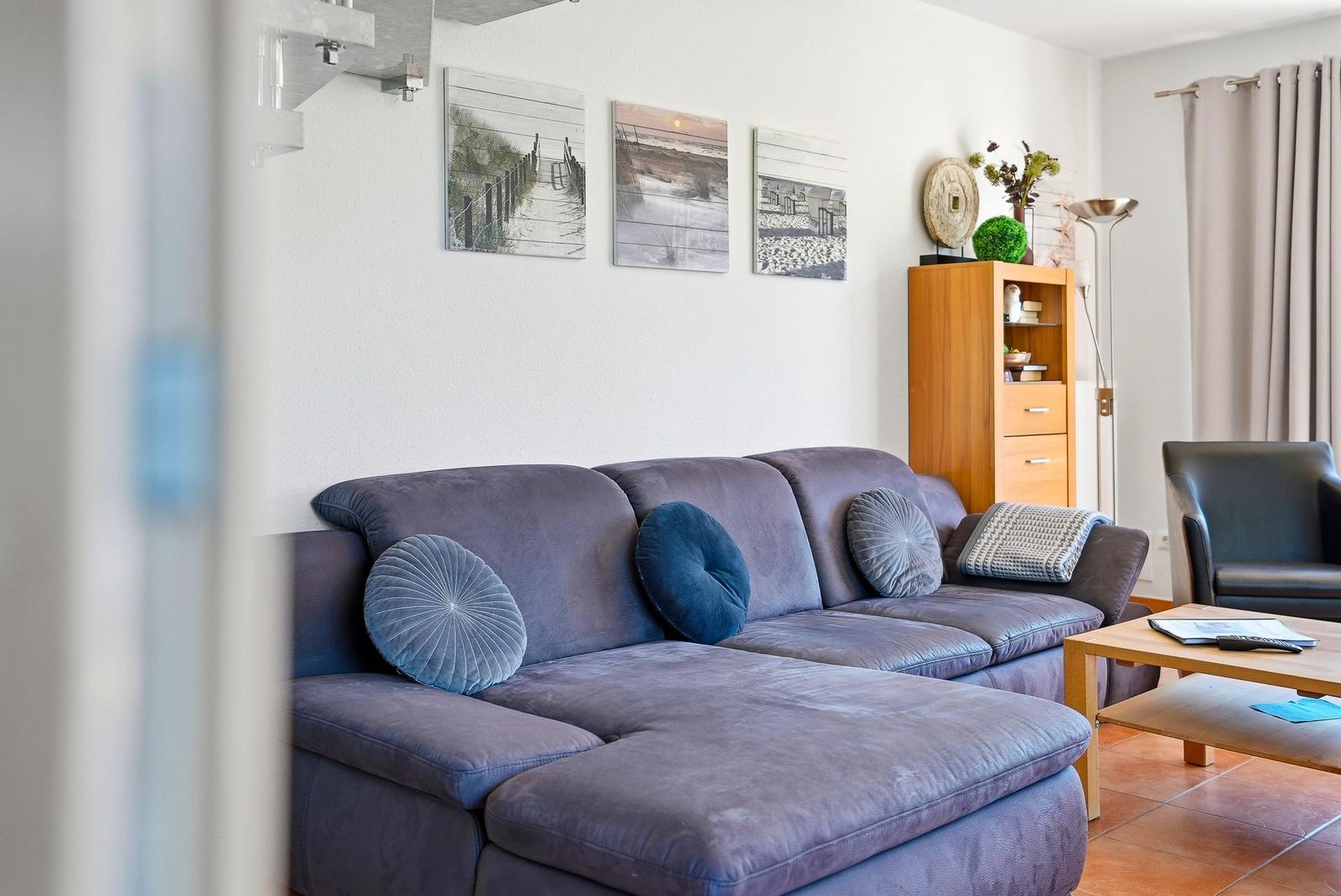 Ein Wohnzimmer mit einem grauen Sofa, Wandbildern und einem Holzregal.