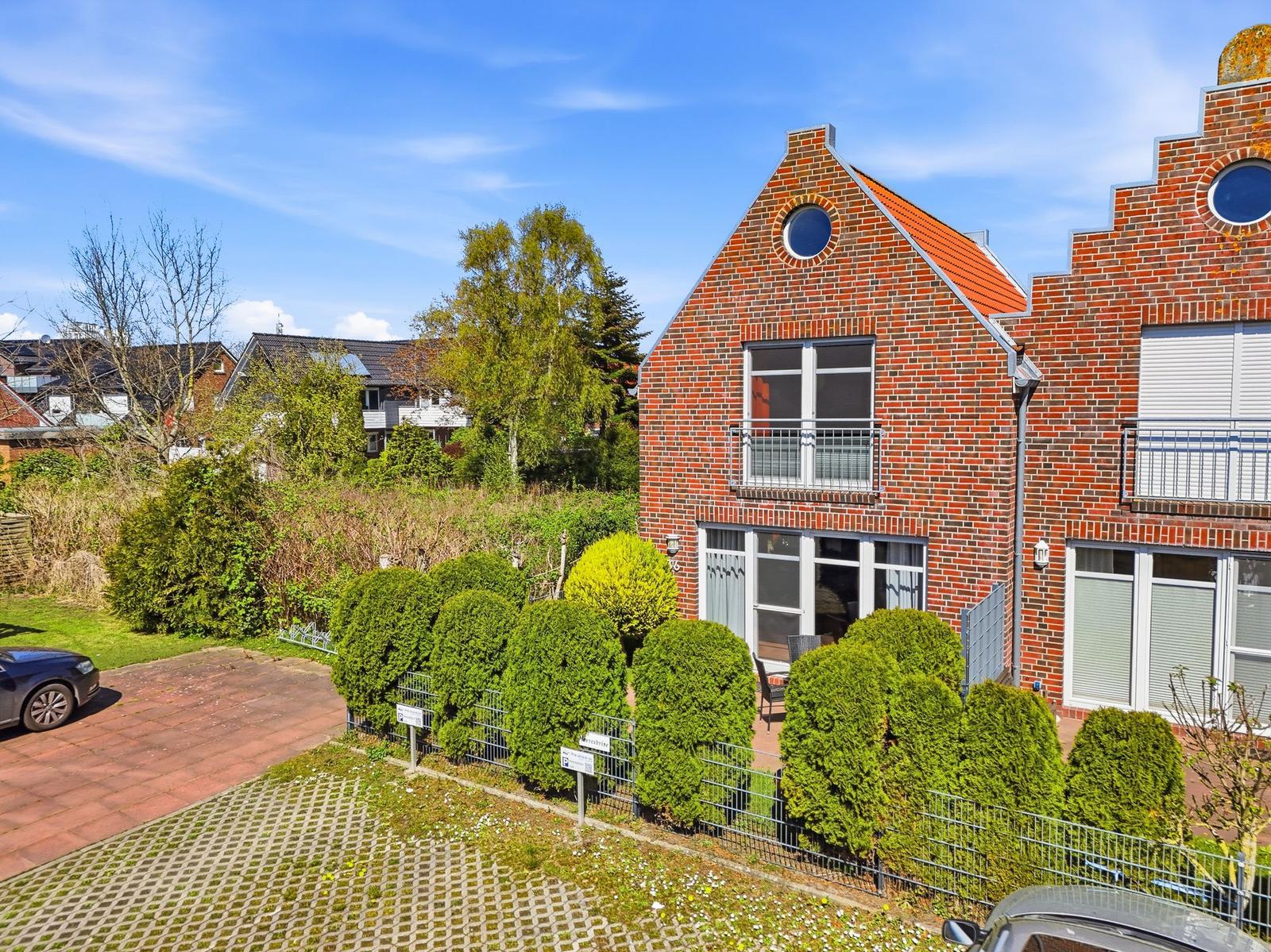 Rotes Backsteingebäude mit Balkon und grüner Hecke im Vorgarten.