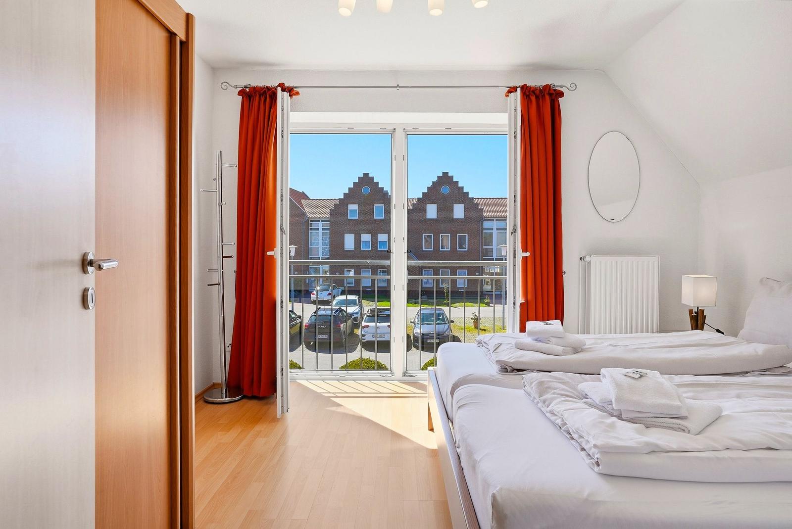 Schlafzimmer mit Doppelbett, roten Vorhängen und Balkonblick auf Gebäude.
