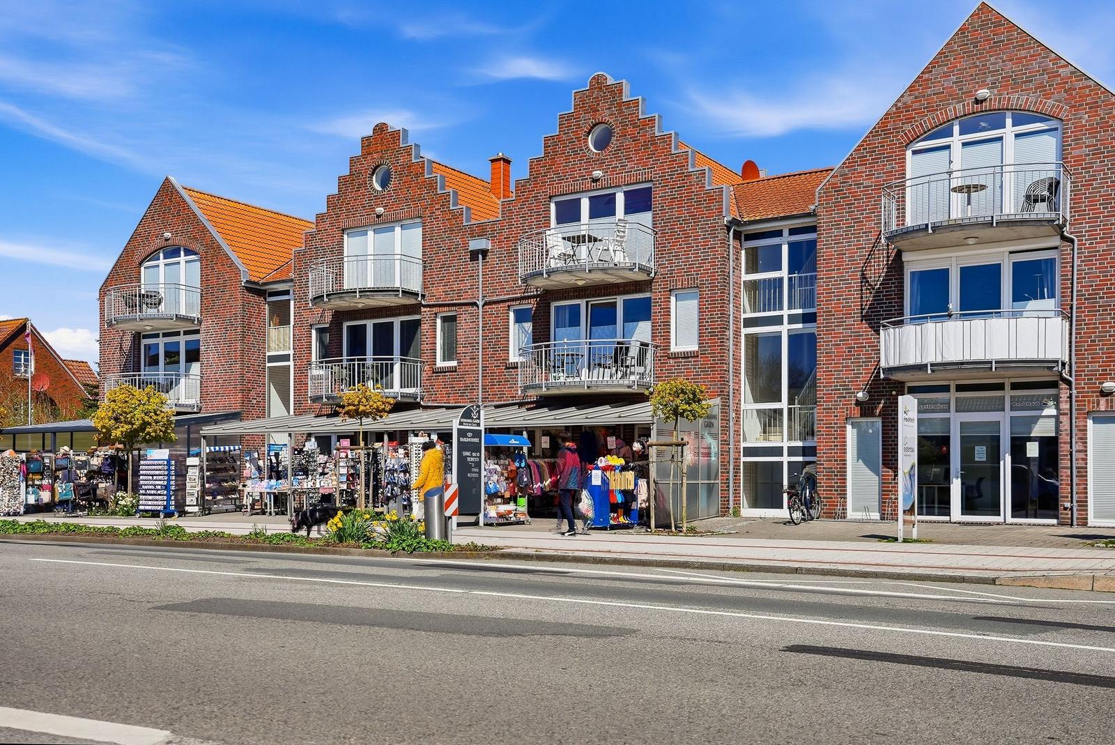 Rotes Backsteingebäude mit Balkonen und Geschäften an der Straße.